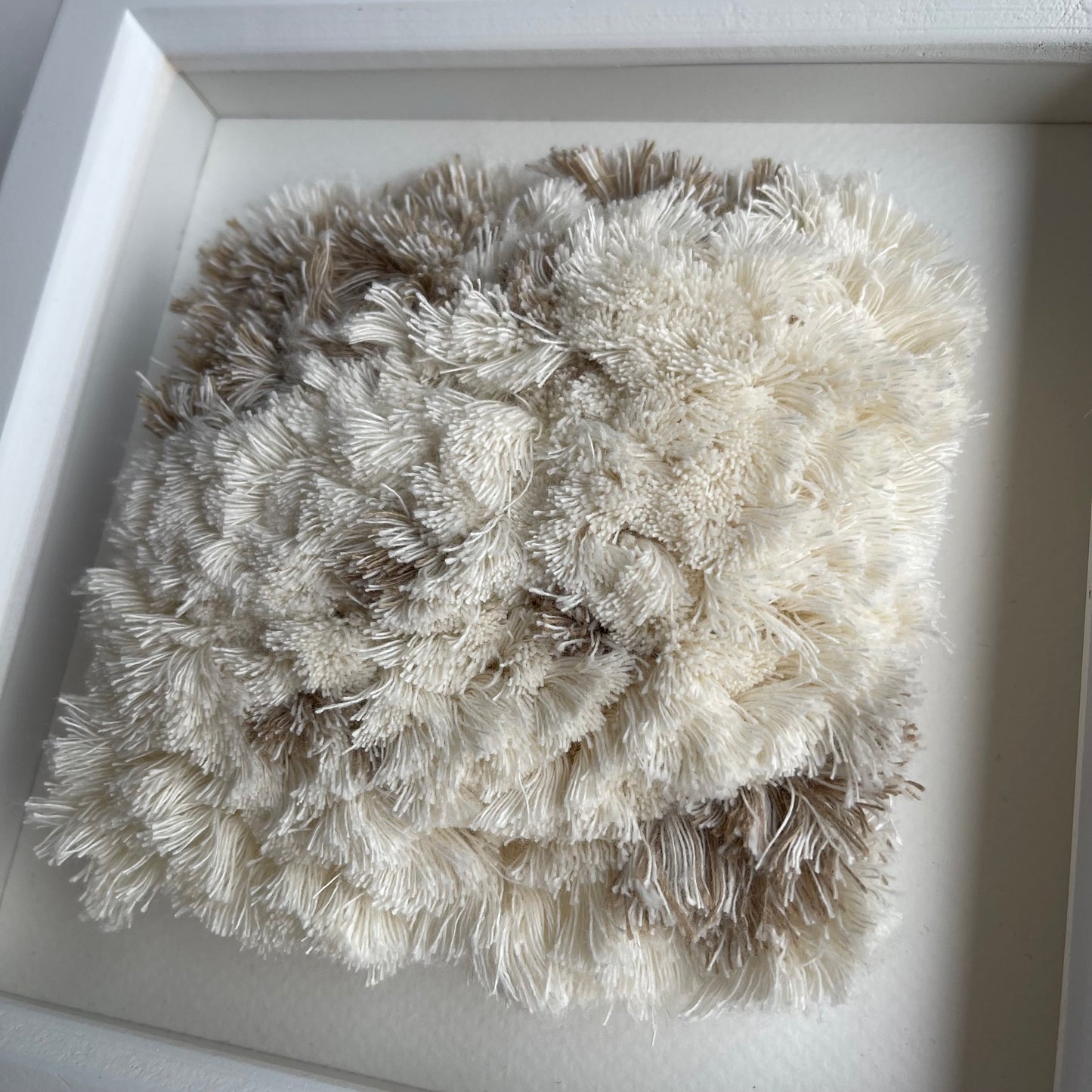 Close up detail of cream and sand fluffy textured woven textile art in square white painted wood frame
