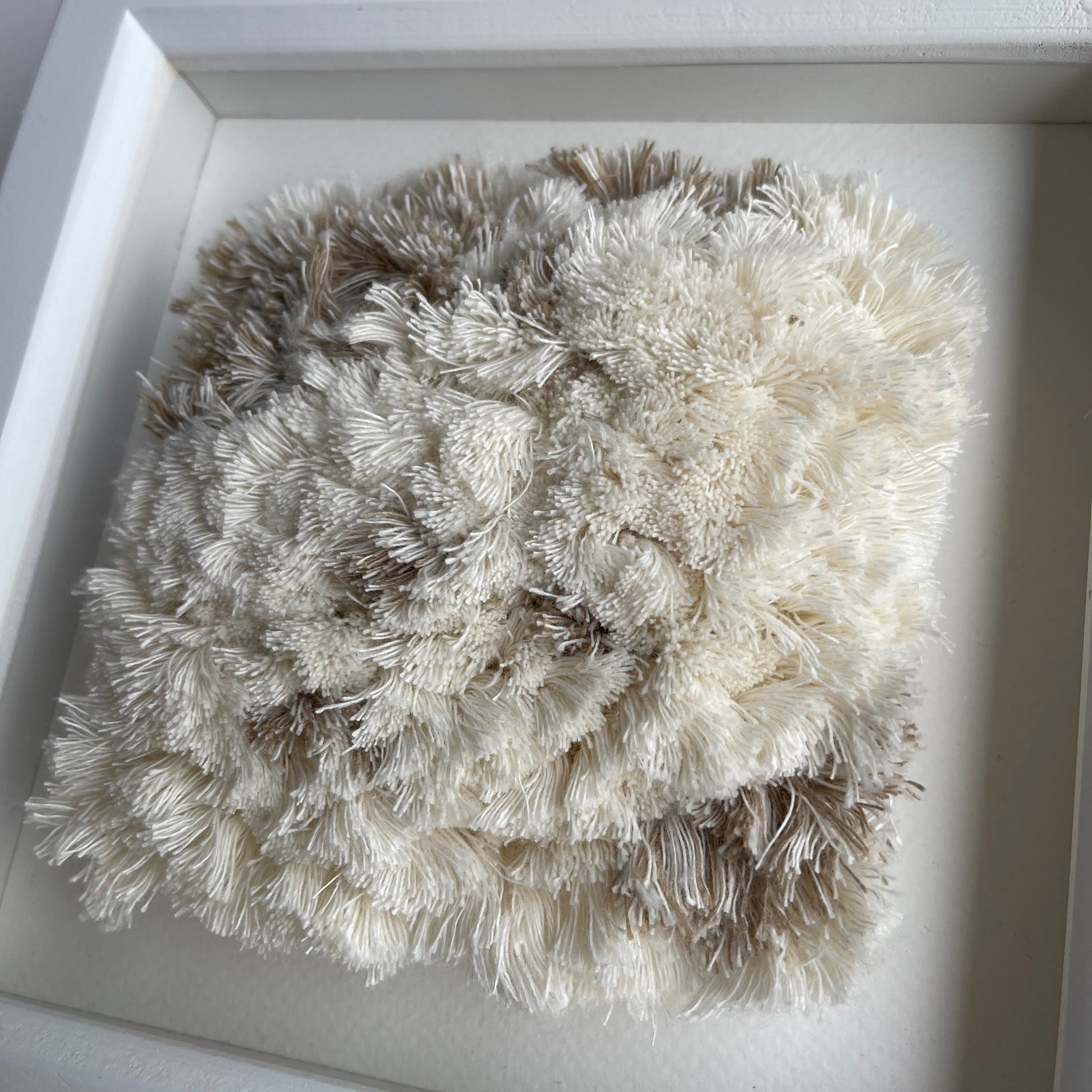 Close up detail of cream and sand fluffy textured woven textile art in square white painted wood frame