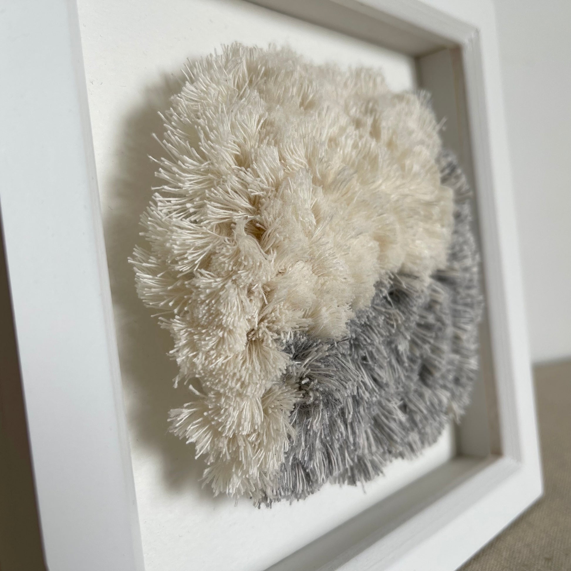 Close up view of blue and cream fluffy textured woven textile art in square white painted wood deep box frame