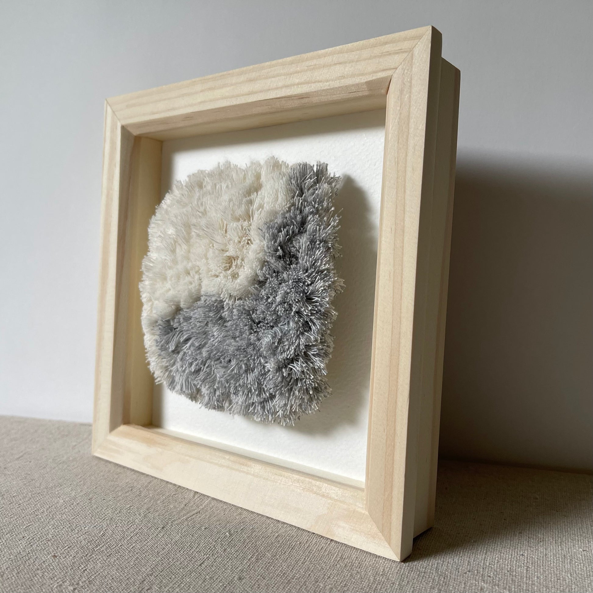 Side view of blue and cream fluffy textured woven textile art in square natural wood frame