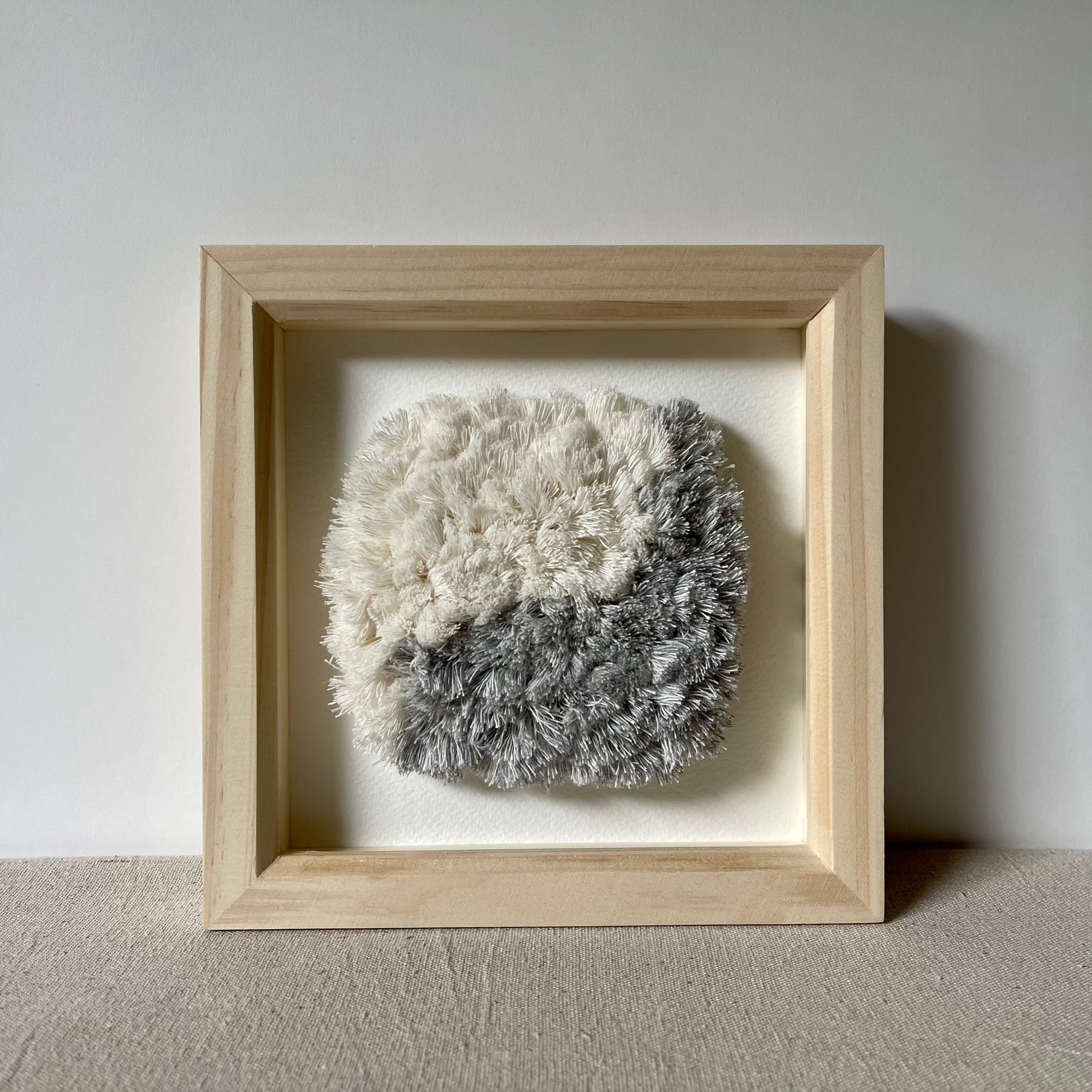 Front view of blue and cream fluffy textured woven textile art in square natural wood deep box frame