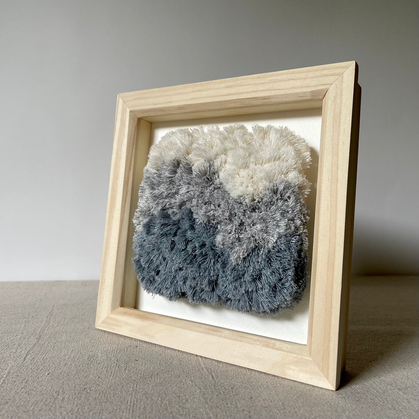Cream and blue fluffy woven textile art in square natural wood box frame