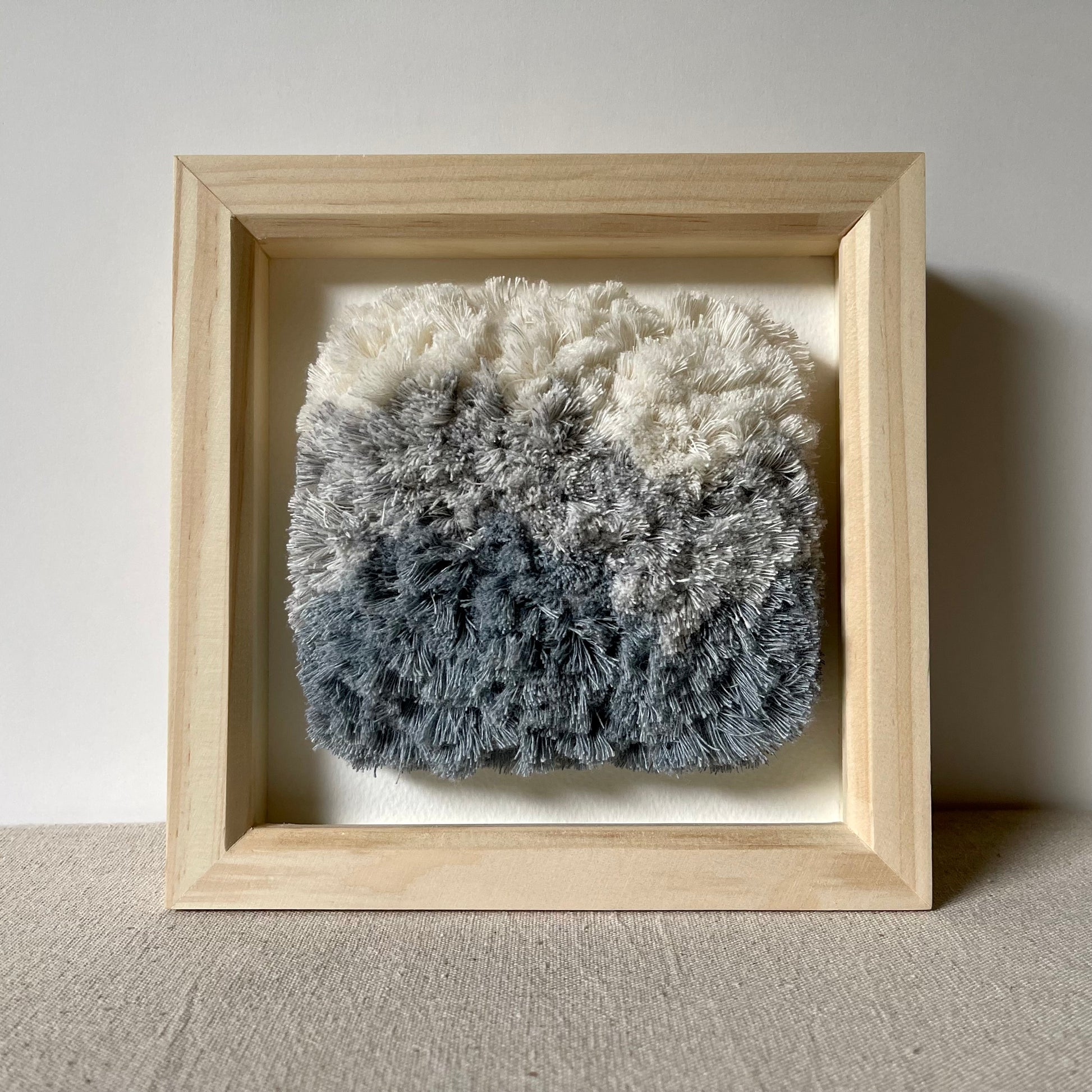 Front view of cream and blue fluffy textured woven textile art in square natural wood deep box frame