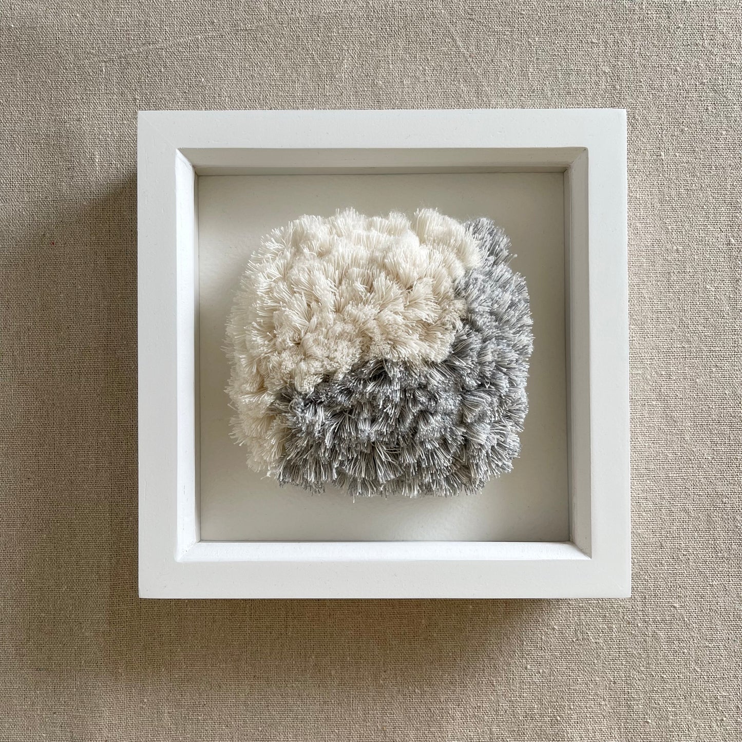 Front view of blue and cream fluffy textured woven textile art in square white painted wood deep box frame