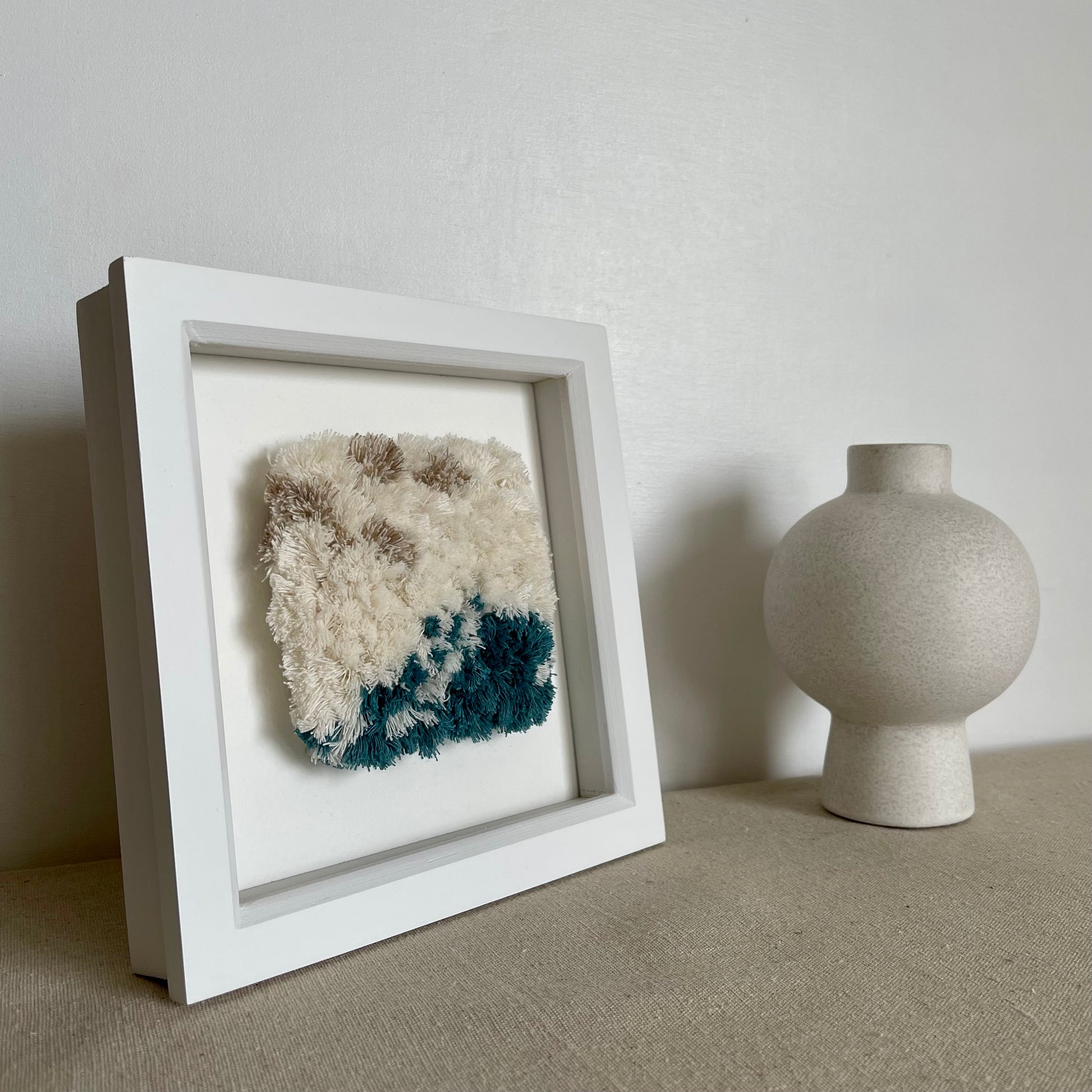 Cream and ocean teal woven fluffy textured  wall art in a square white painted wood deep box frame next to scandi vase