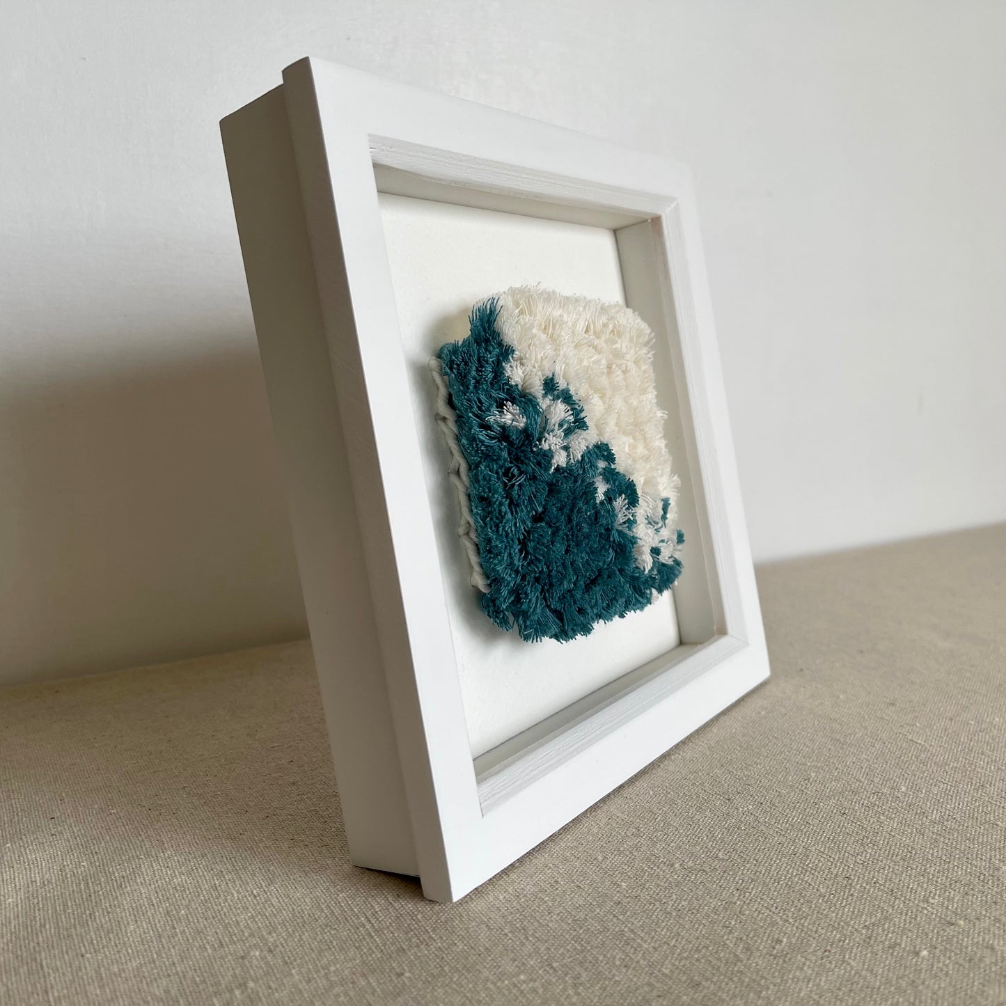 Side view of teal and cream fluffy textured woven textile art in a square white painted wood deep box frame