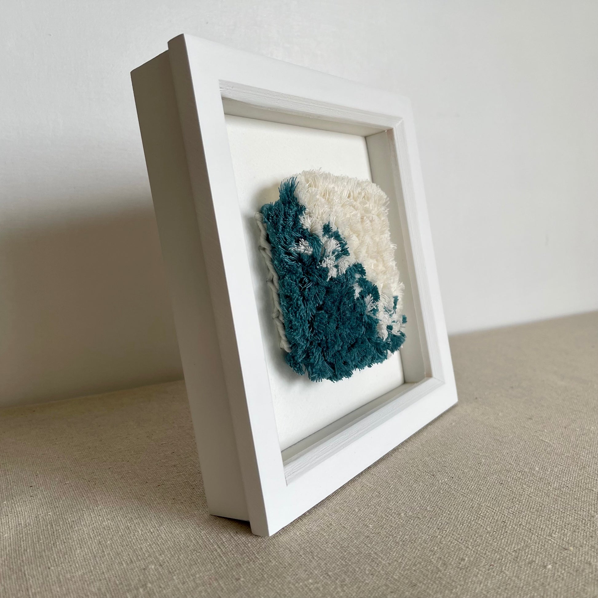 Side view of teal and cream fluffy textured woven textile art in a square white painted wood deep box frame