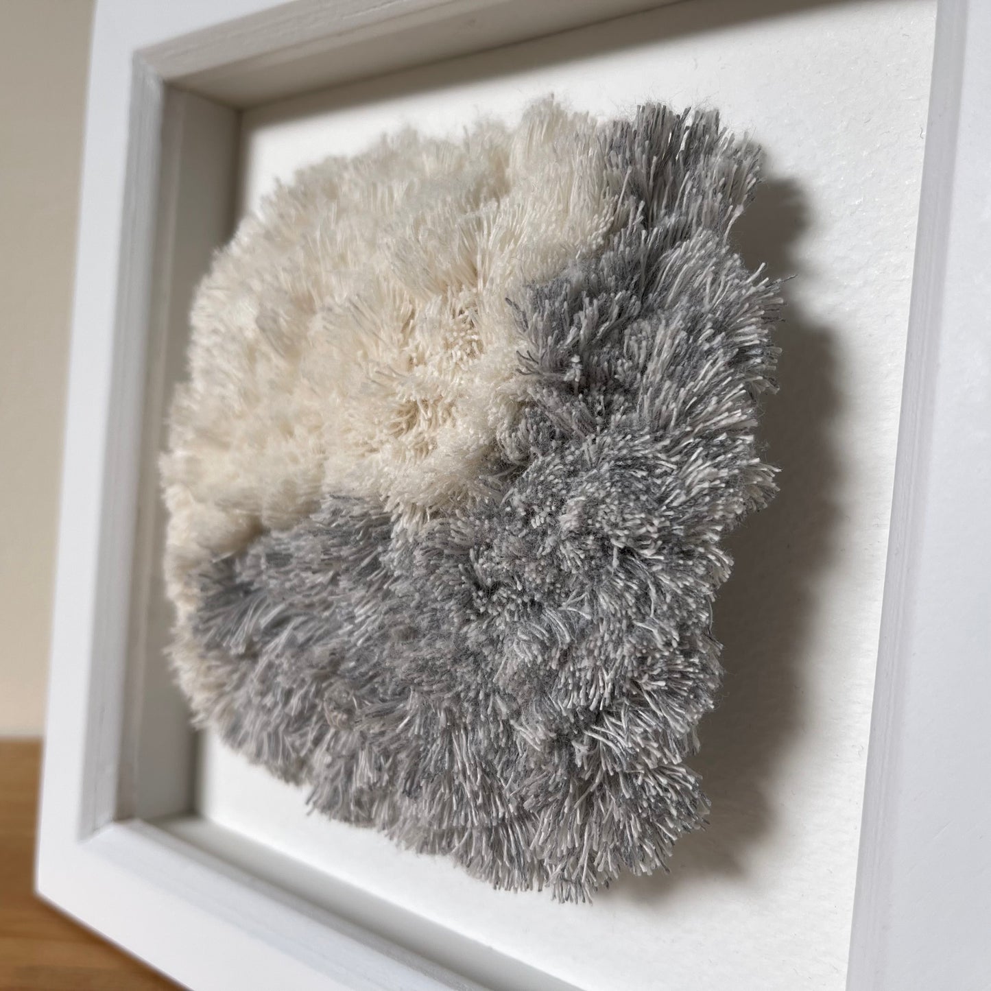 Close up detail of blue and cream fluffy textured woven textile art in square white painted wood frame