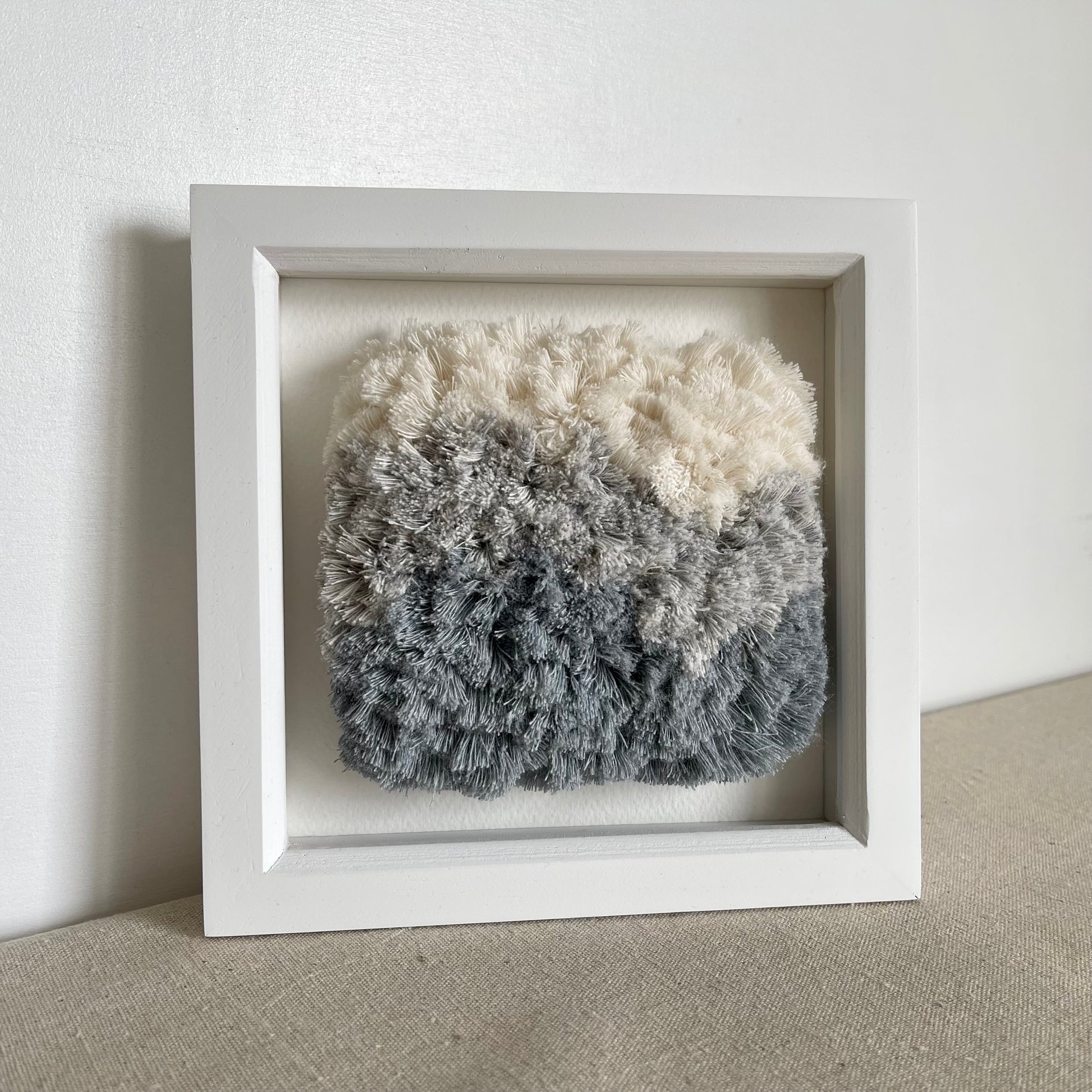Cream and blue fluffy textured woven textile art in square white painted wood frame