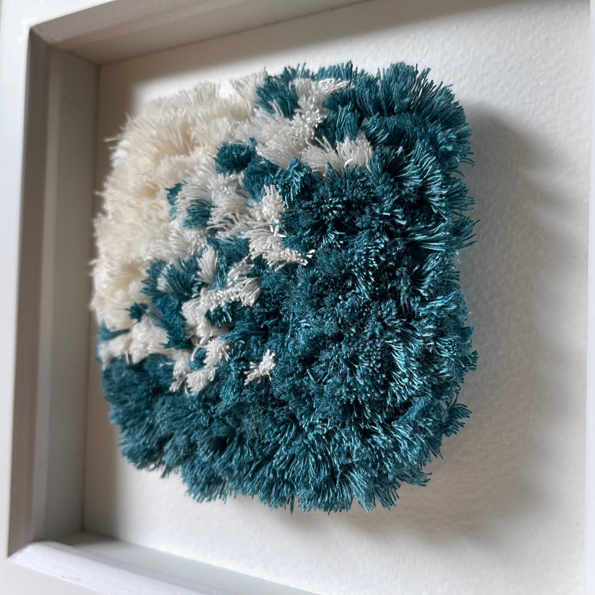 Close up detail of ocean teal and cream fluffy textured woven wall art in a square white painted wood deep box frame
