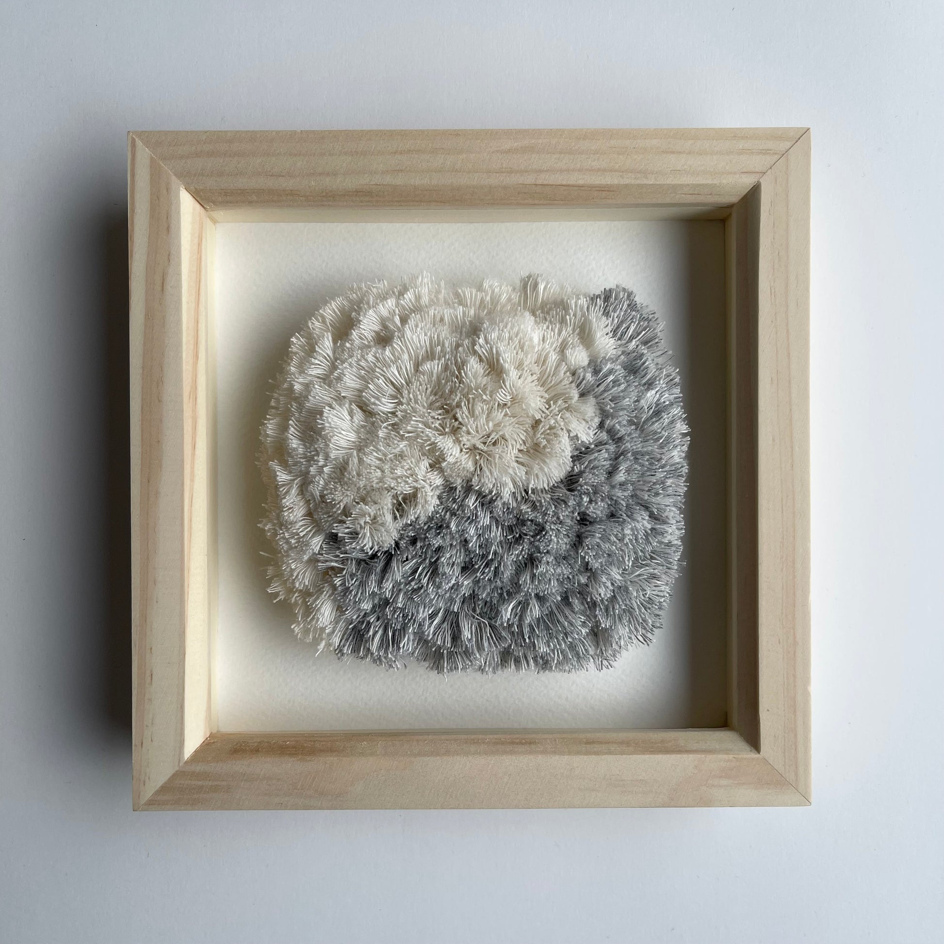 Front view of blue and cream fluffy textured woven textile art in square natural wood deep box frame on wall