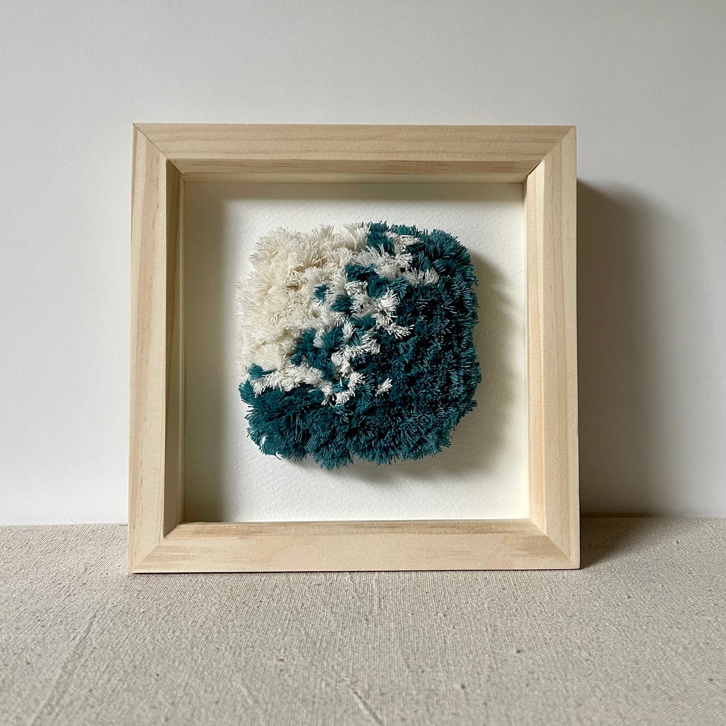 Front view of ocean teal and cream fluffy textured woven art in a square wood deep box frame