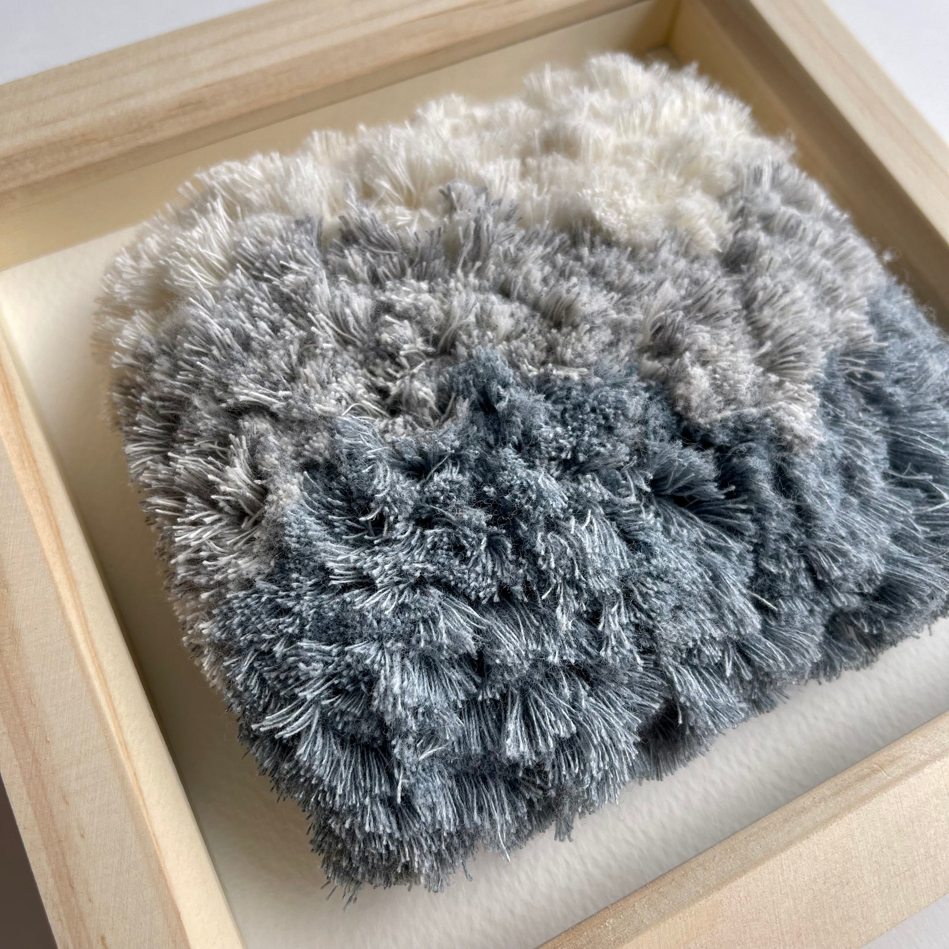 Close up detail of cream and blue fluffy textured woven textile art in square natural wood deep box frame