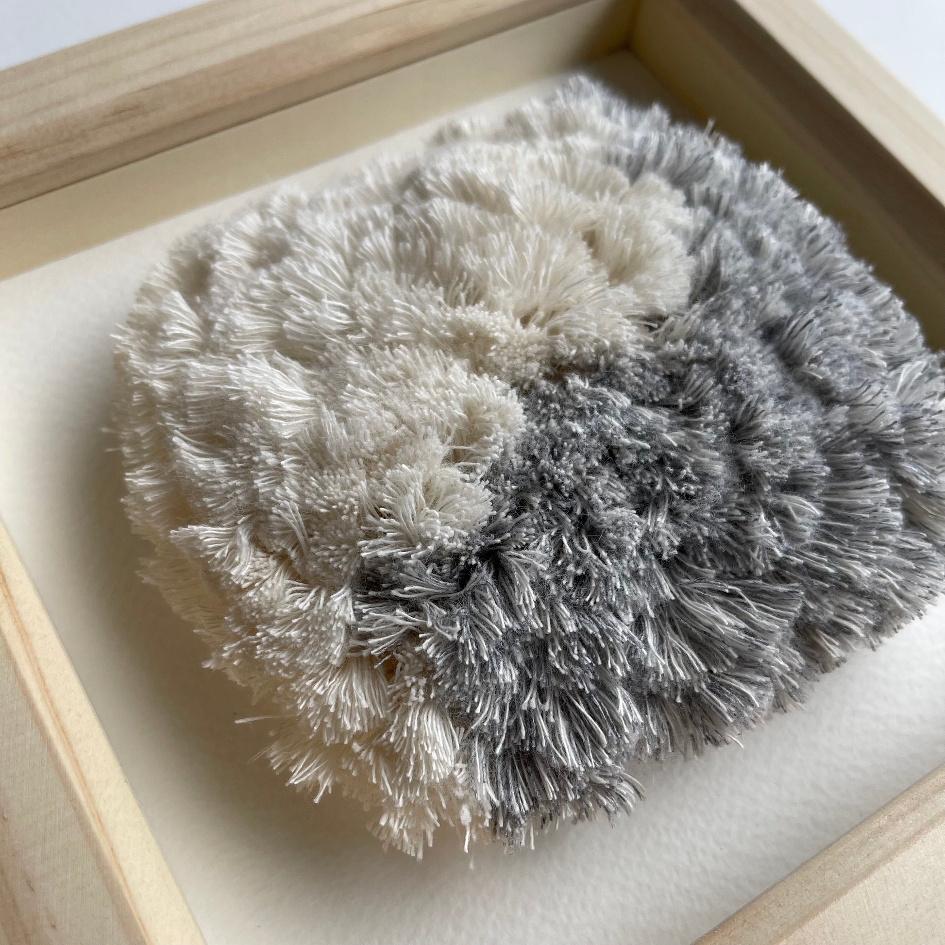 Close up detail of blue and cream fluffy textured woven textile art in square natural wood deep box frame