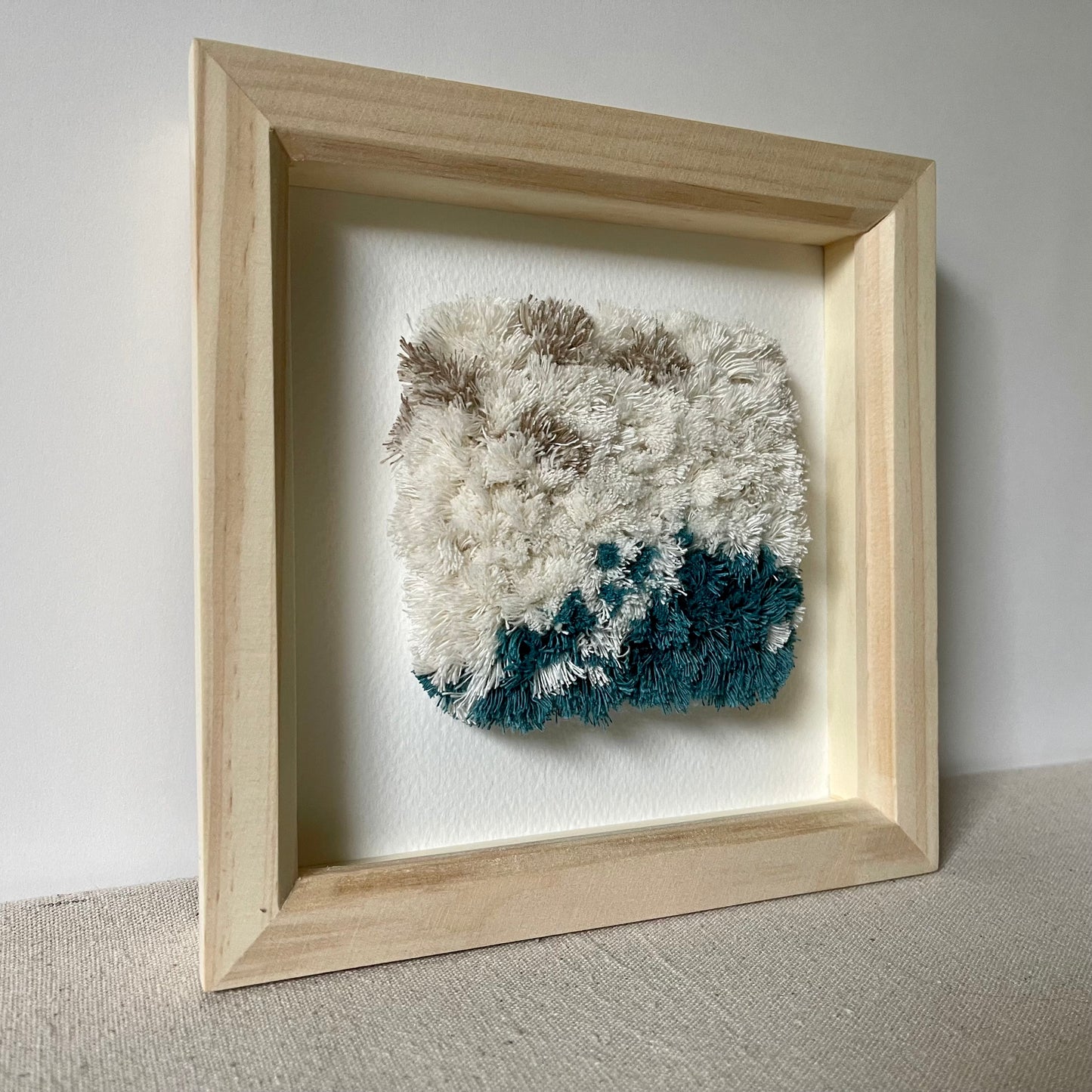 Framed cream and ocean teal woven fluffy textured art in a square natural wood deep box frame