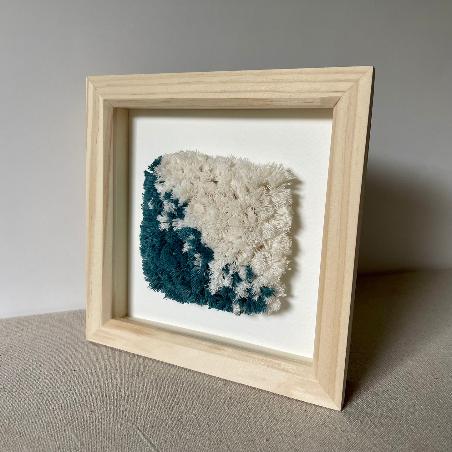 Teal and cream fluffy textured woven textile art in a square natural wood frame