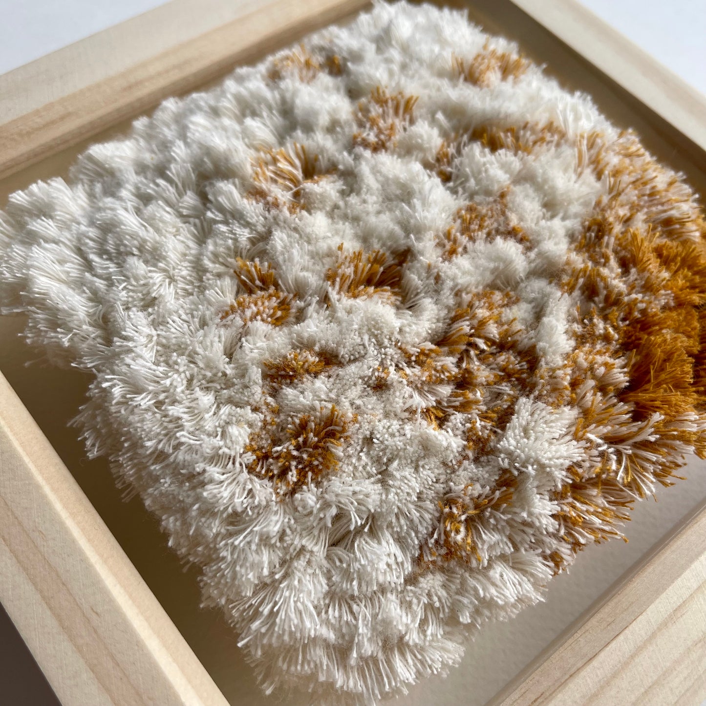Close up detail of cream and yellow ochre fluffy textured woven textile art in natural wood deep box frame