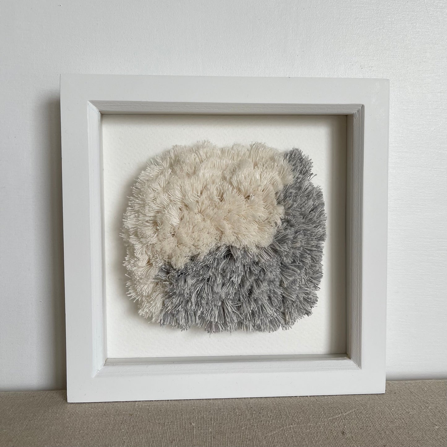 Framed blue and cream textured woven textile art in square white painted wood deep box frame