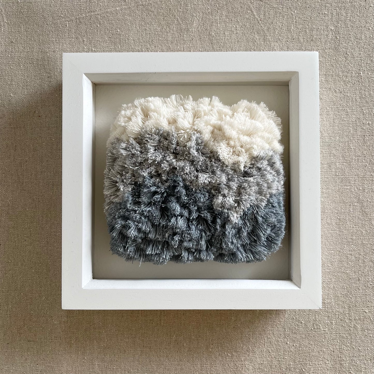 Square framed cream and blue fluffy textured woven textile art in white painted wood frame