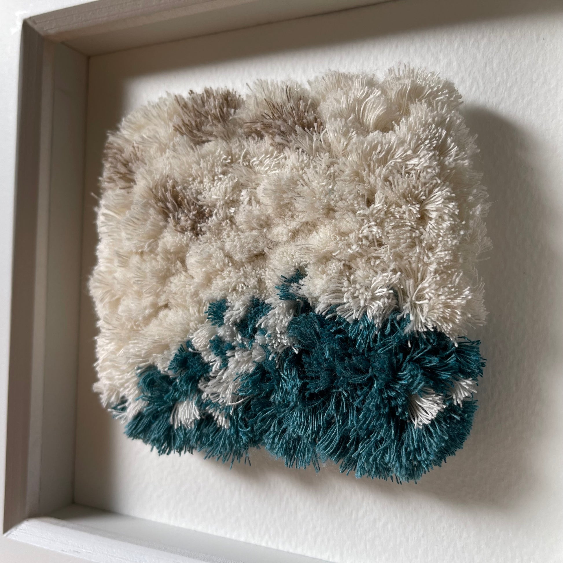 Close up detail of cream and ocean teal woven fluffy textured  art in a square white frame