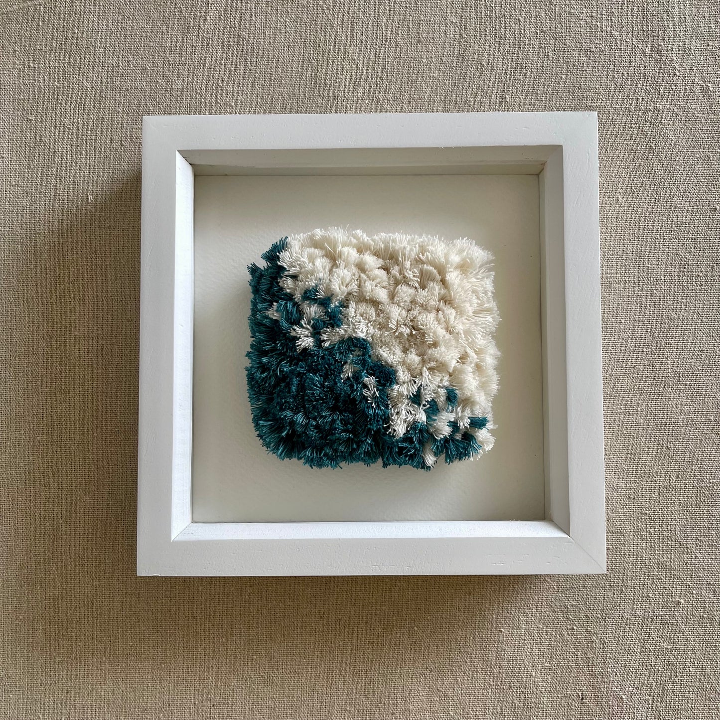 Front view of teal and cream fluffy textured woven textile art in a square white painted wood deep box frame