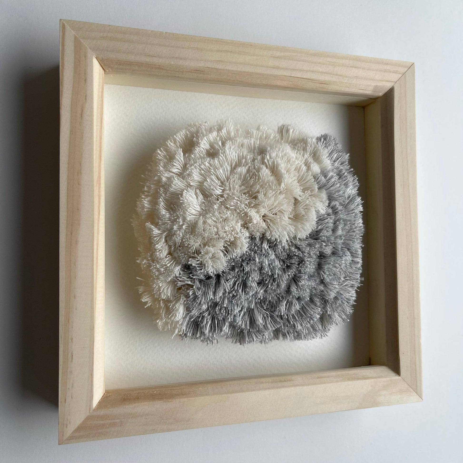 Angled view of blue and cream textured woven textile art in square natural wood deep box frame on wall