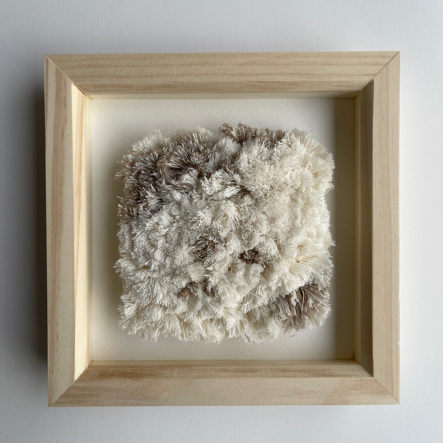 Cream and beige fluffy textured woven textile art in square natural wood deep box frame on wall