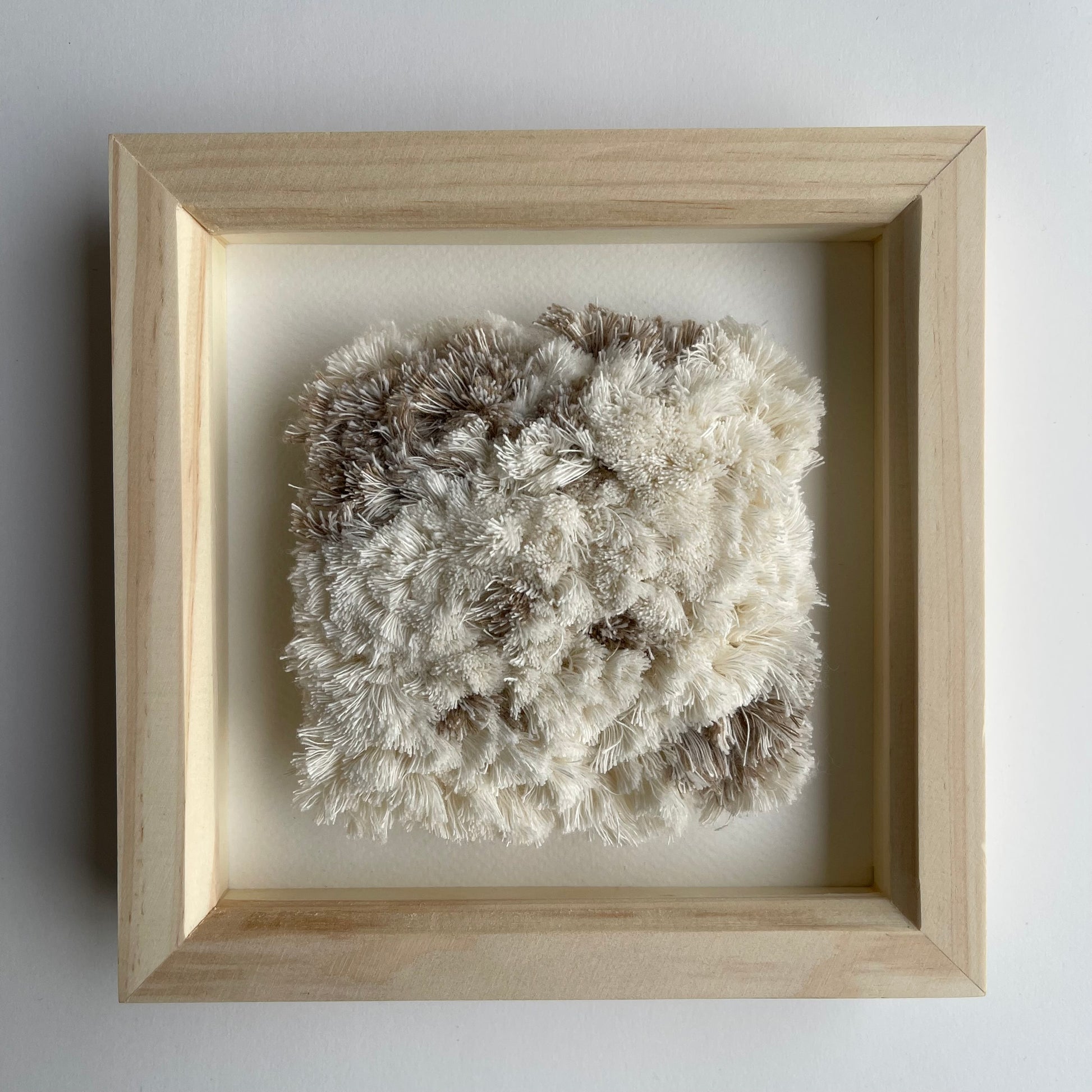 Cream and beige fluffy textured woven textile art in square natural wood deep box frame on wall