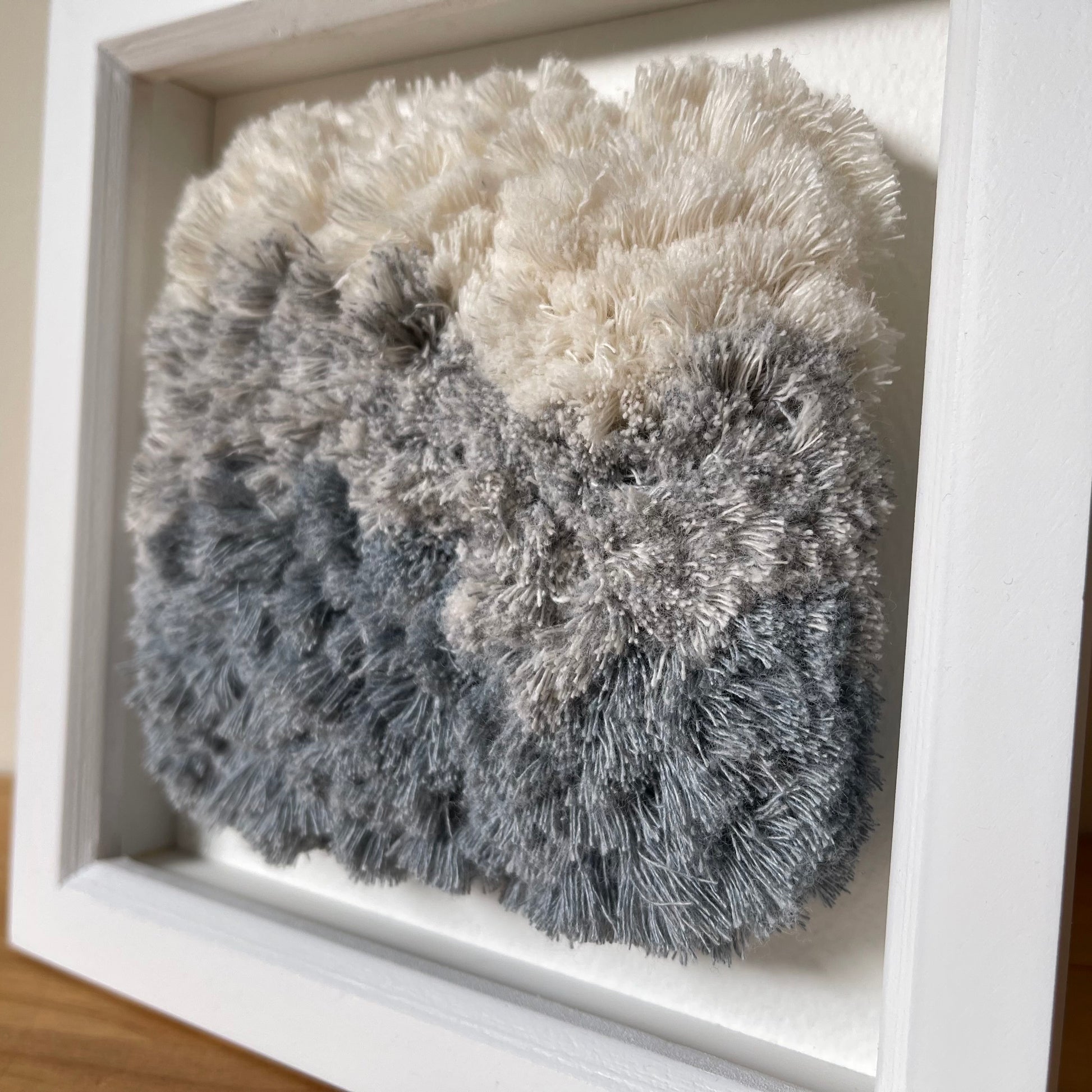 Close up detail of blue and cream fluffy textured woven textile art in square white painted wood deep box frame