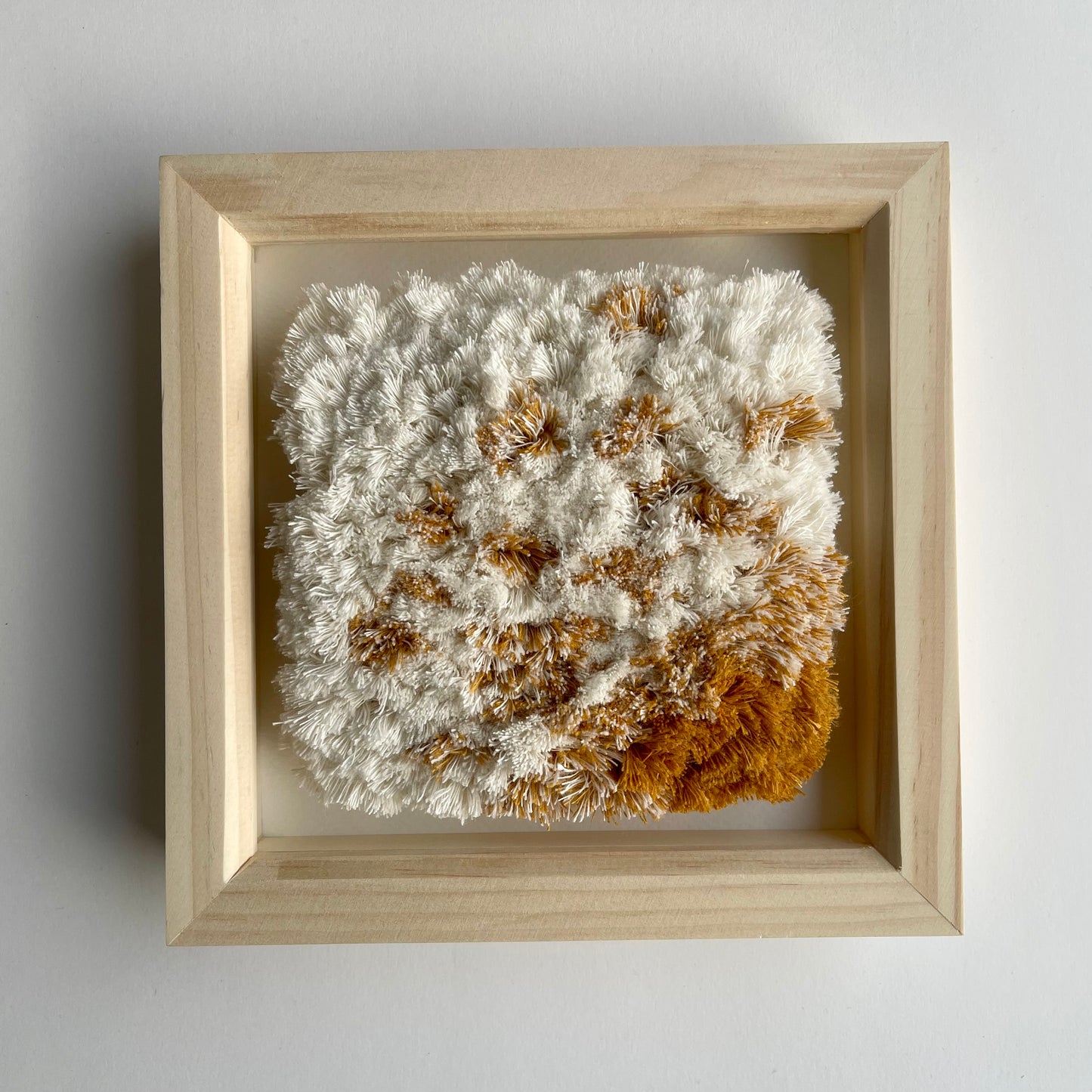 Front view of cream and yellow ochre fluffy textured woven textile art in natural wood deep box frame on wall