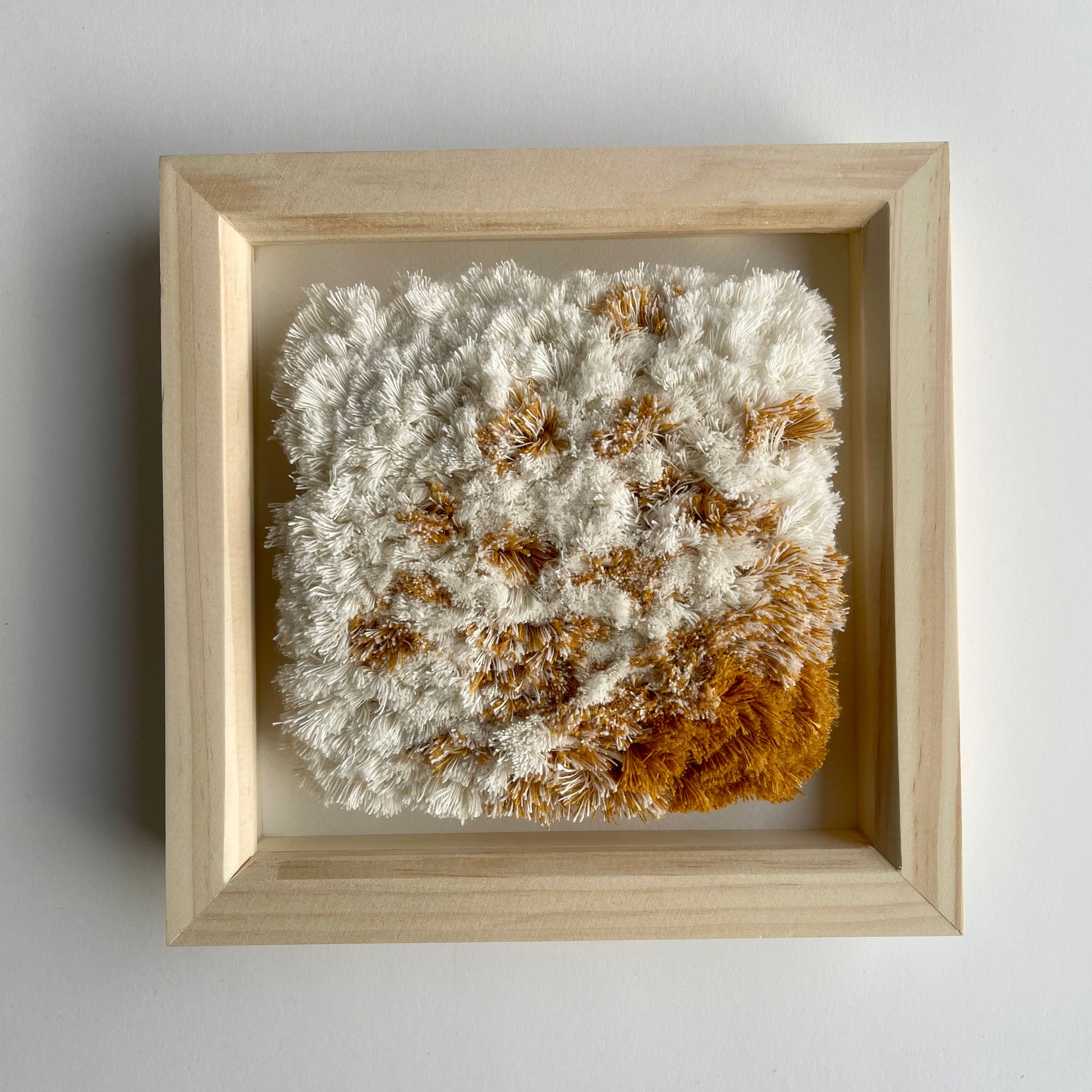Front view of cream and yellow ochre fluffy textured woven textile art in natural wood deep box frame on wall