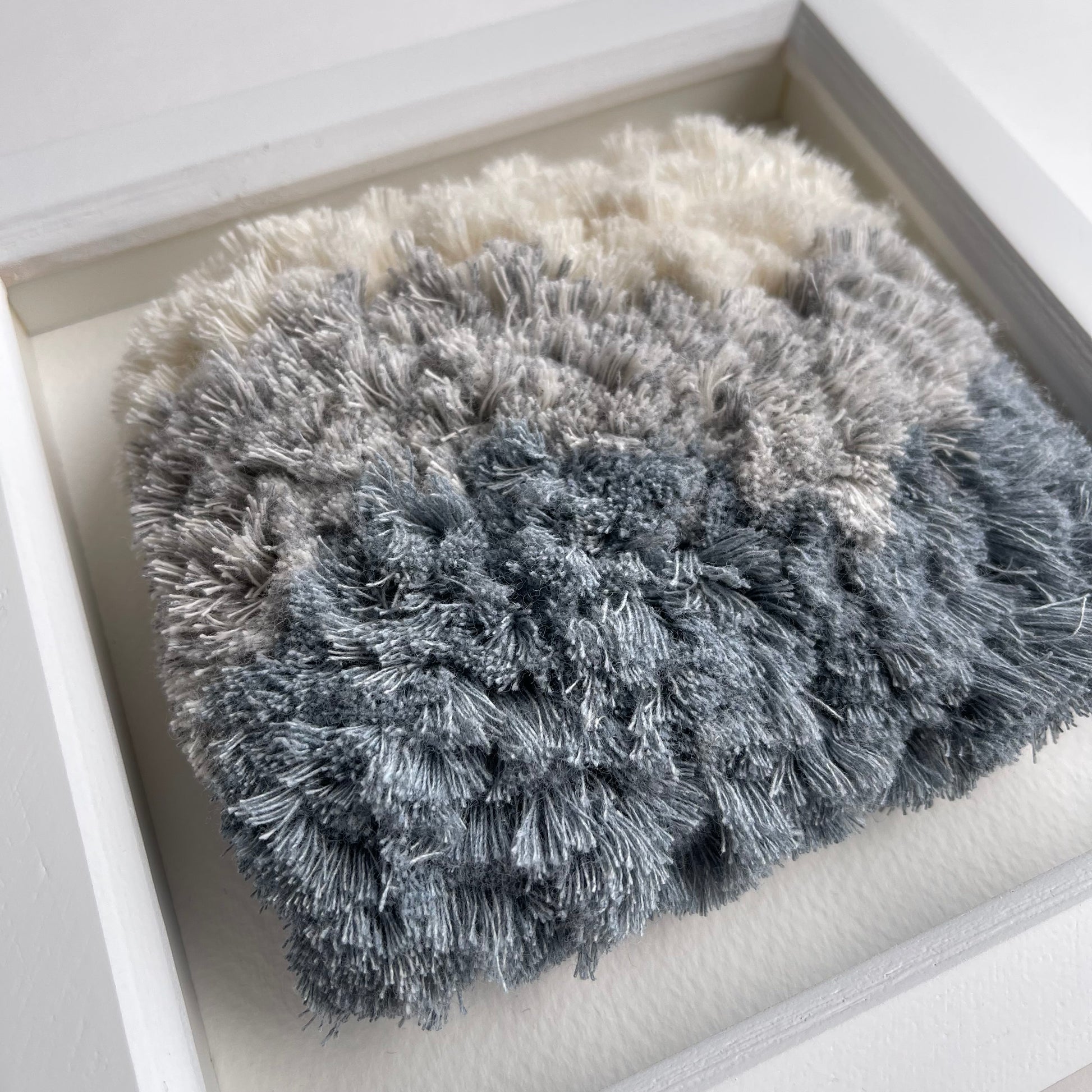 Angled close up of cream and blue fluffy textured woven textile art in square white frame
