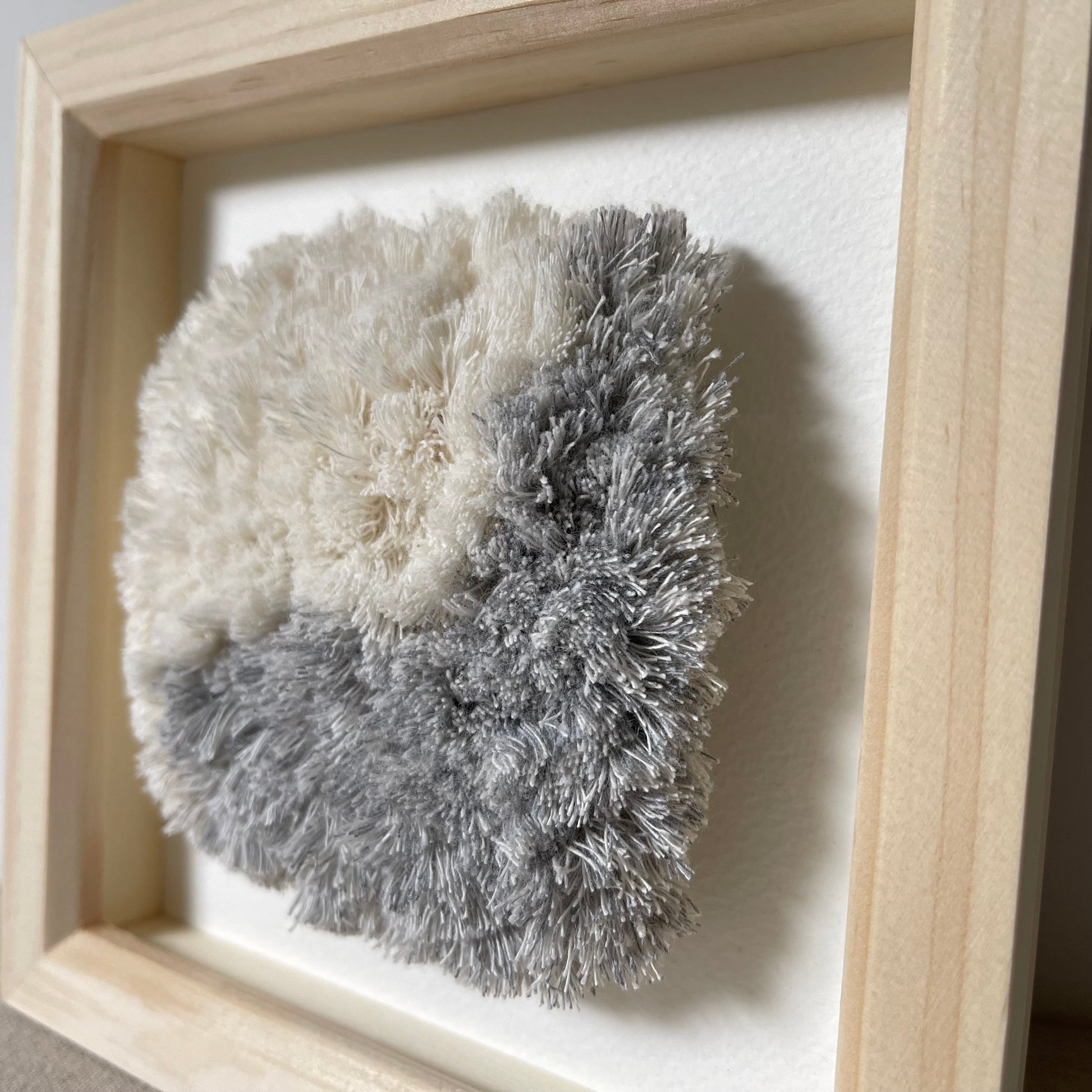Close up view of blue and cream fluffy woven textile art in square natural wood deep box frame