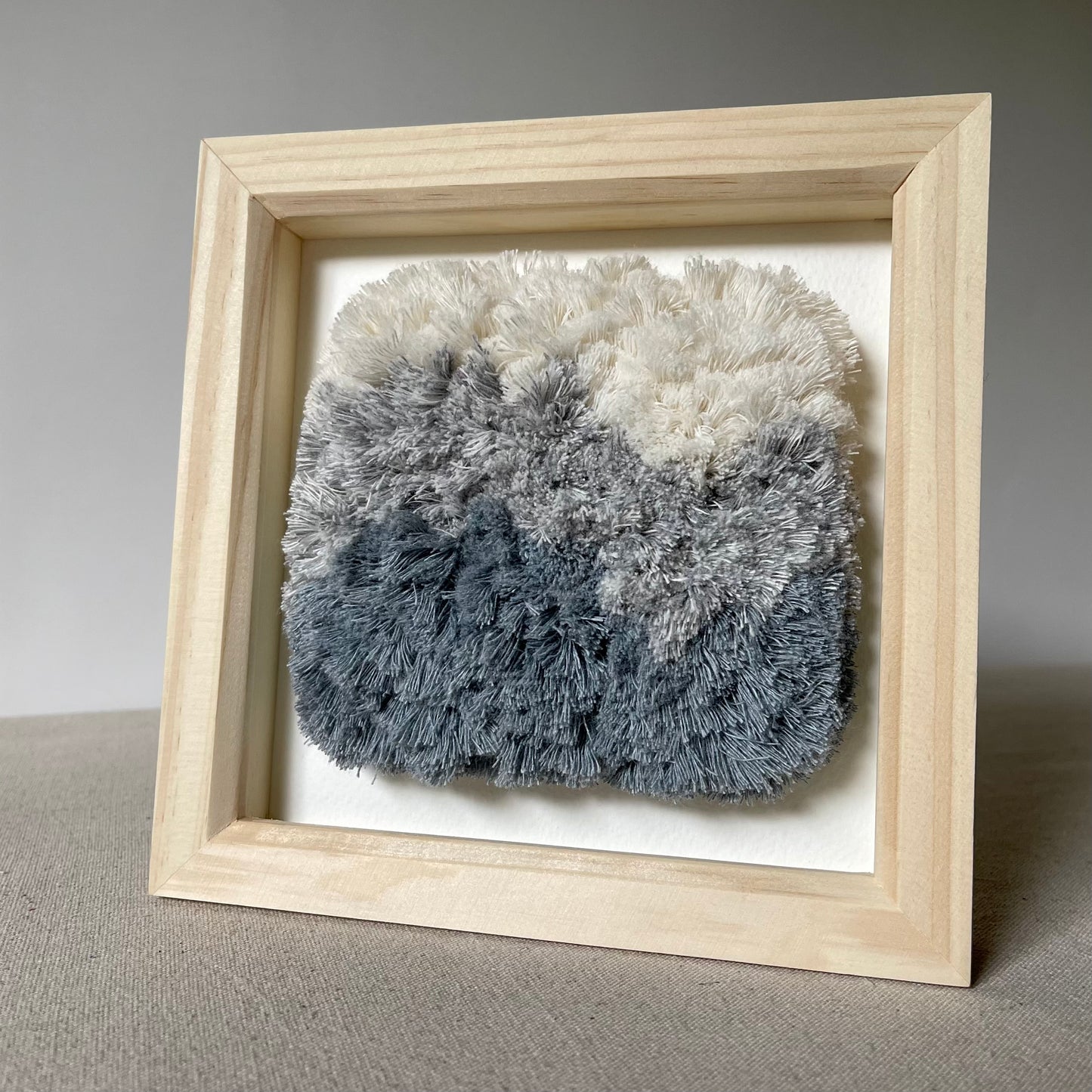 Cream and blue fluffy textured woven textile art in square natural wood deep box frame
