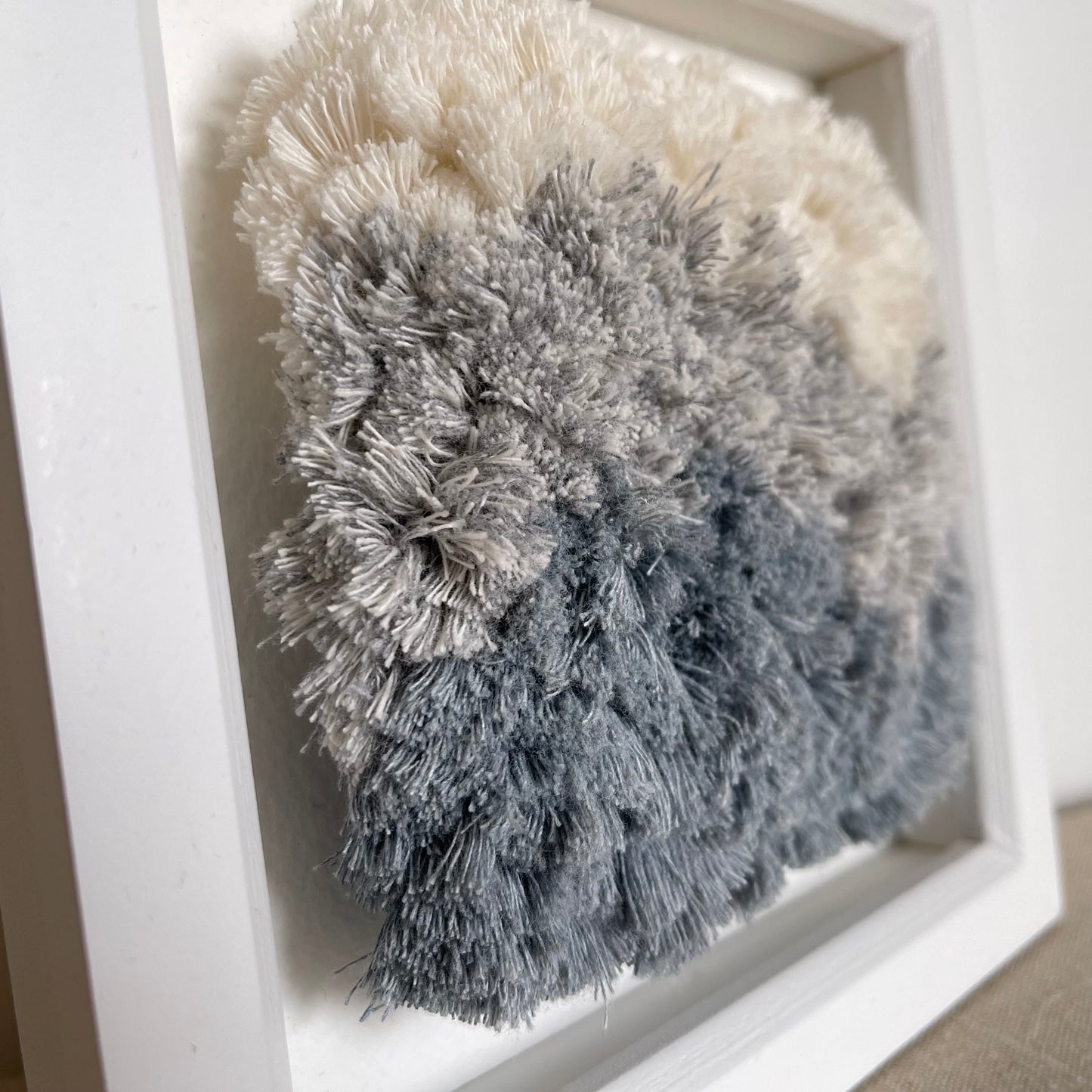 Close up detail of cream and blue fluffy cotton woven textile art in square white painted wood deep box frame