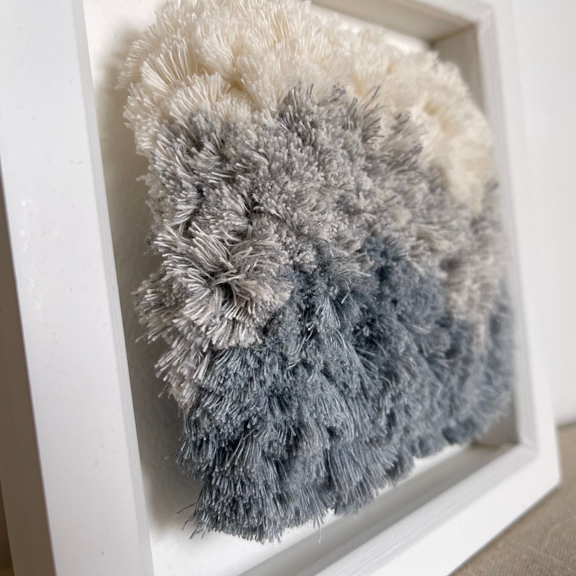 Close up detail of cream and blue fluffy cotton woven textile art in square white painted wood deep box frame