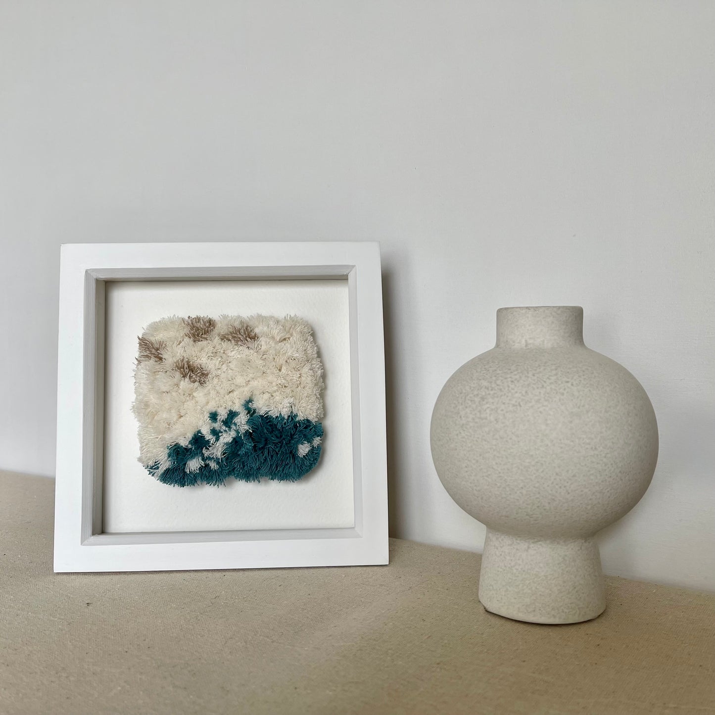 Cream and ocean teal woven fluffy art in a square white painted wood frame