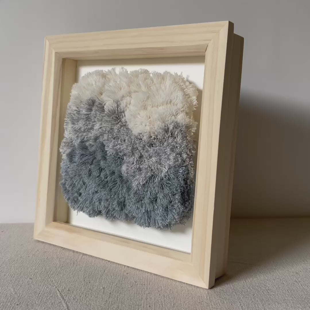 Video of cream and blue fluffy textured woven textile art in square natural wood deep box frame