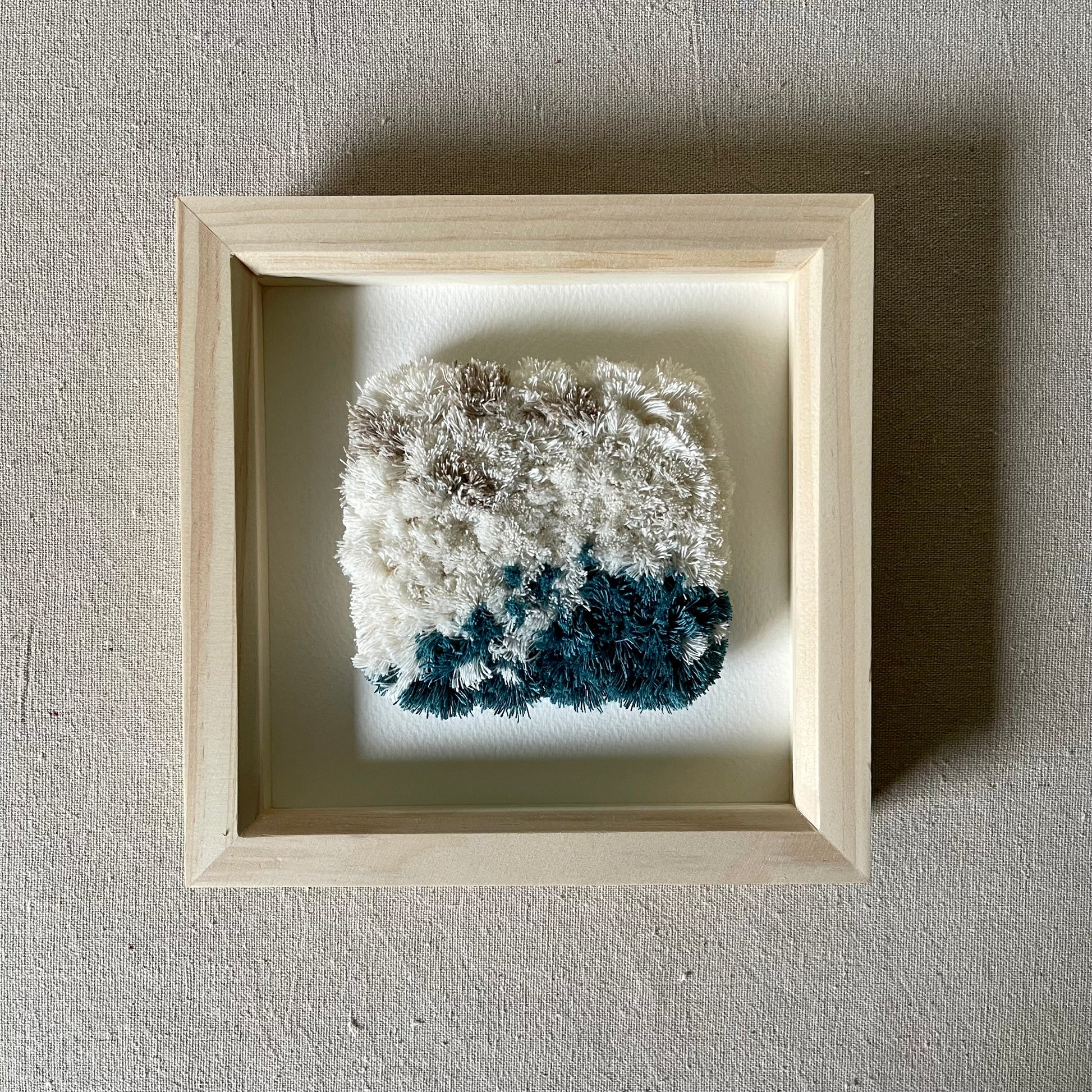 Front view of cream and ocean teal woven fluffy textured  wall art in a square wood deep box frame