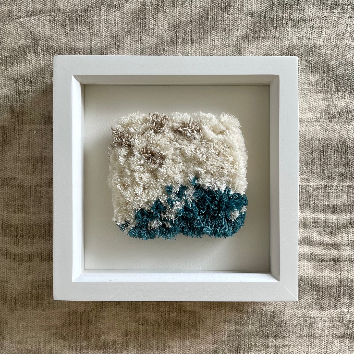 Front view of cream and ocean teal woven fluffy textured  wall art in a square white painted wood deep box frame