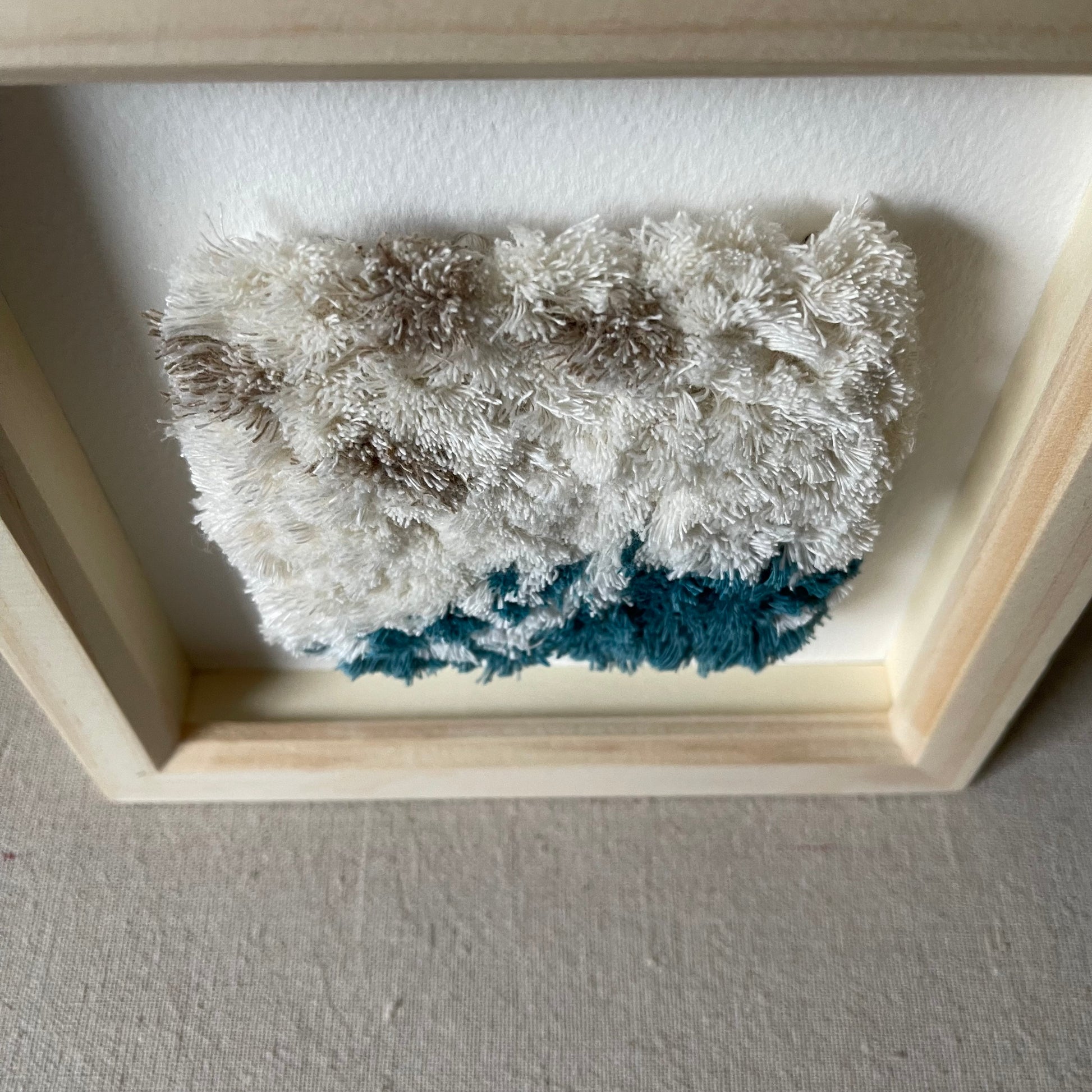 Top view of cream and ocean teal woven fluffy textured art in a square wood deep box frame