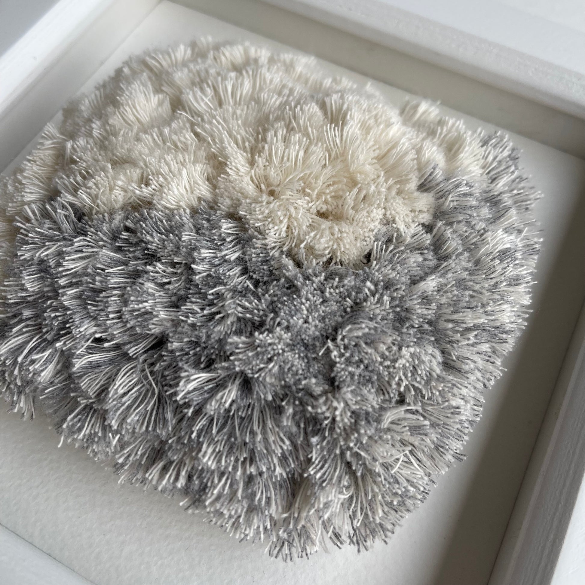 Angled close up of blue and cream fluffy textured woven textile art in square white painted wood frame