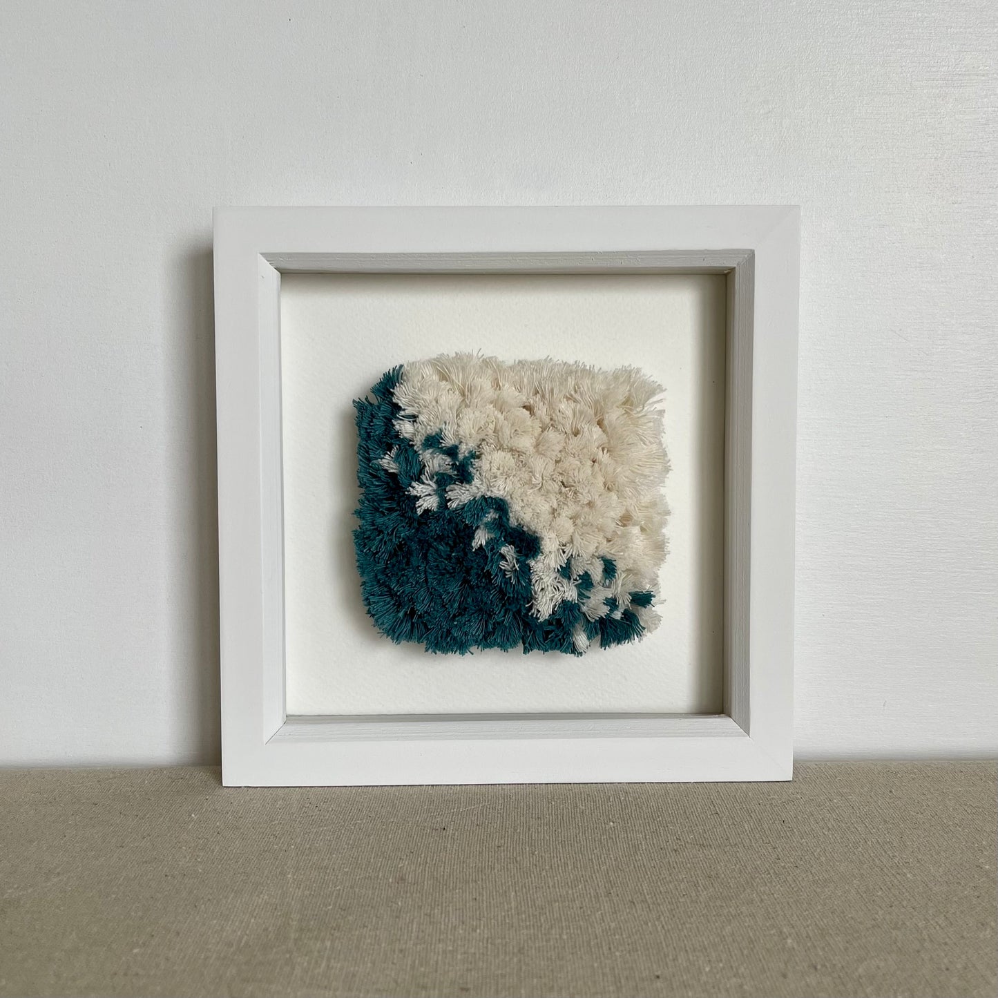 Square white painted wood deep box frame housing teal and cream fluffy textured woven textile art