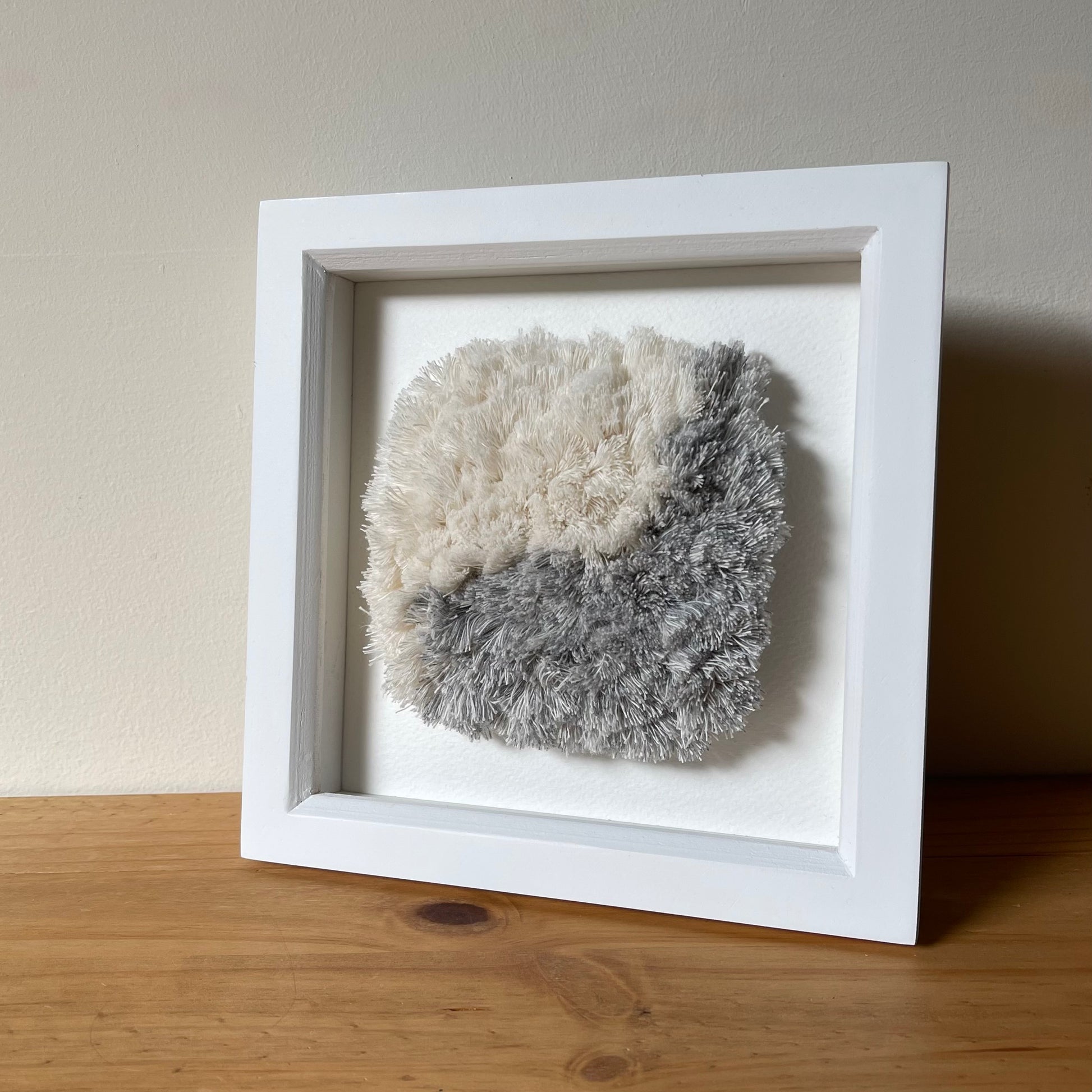 Square white painted wood box frame showcasing a blue and cream fluffy textured woven textile art piece
