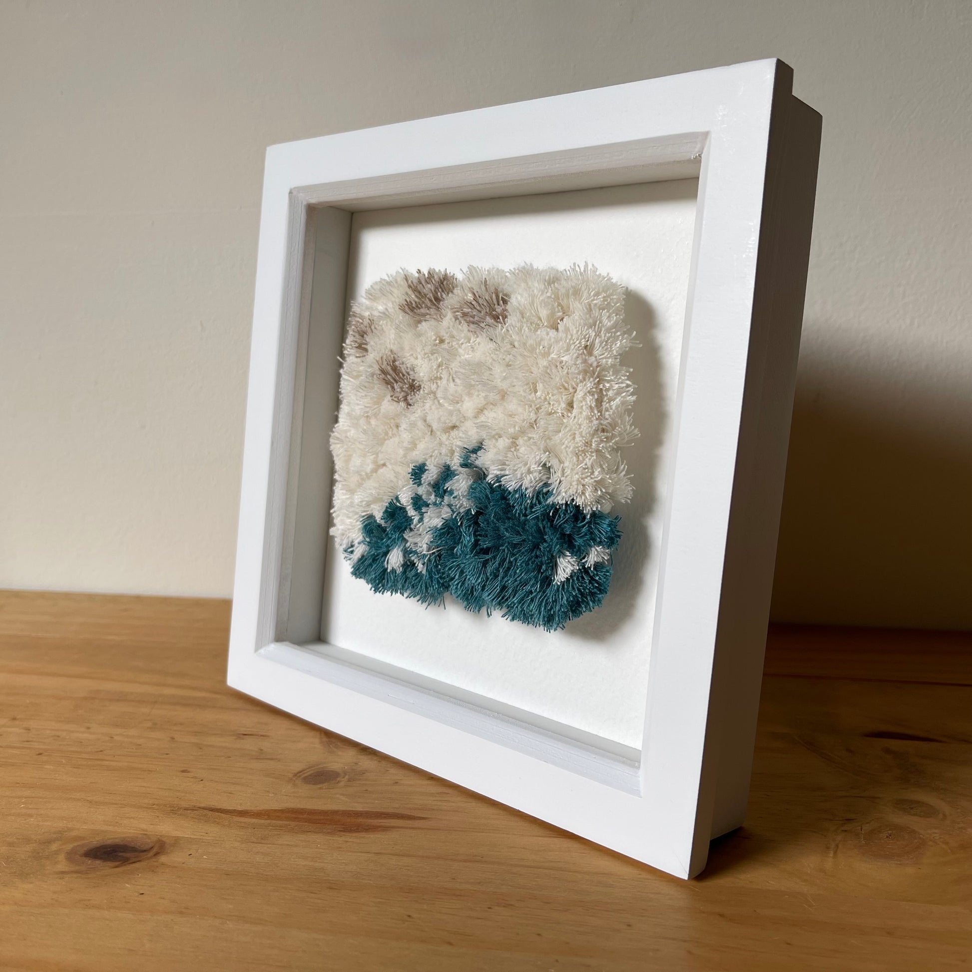 Cream and ocean teal woven fluffy textile  art in a square white painted wood deep box frame
