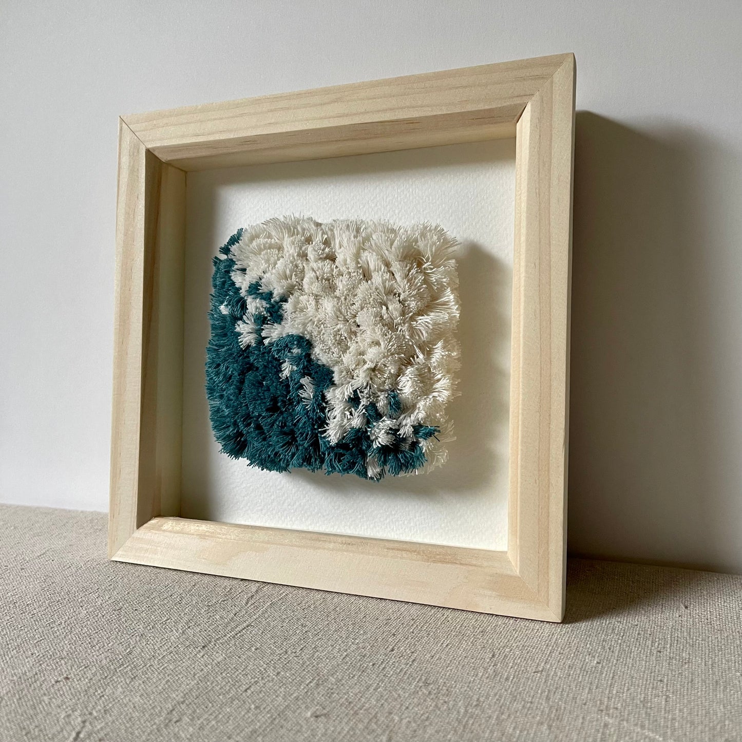 Teal and cream hand woven textile art in a square natural wood deep box frame
