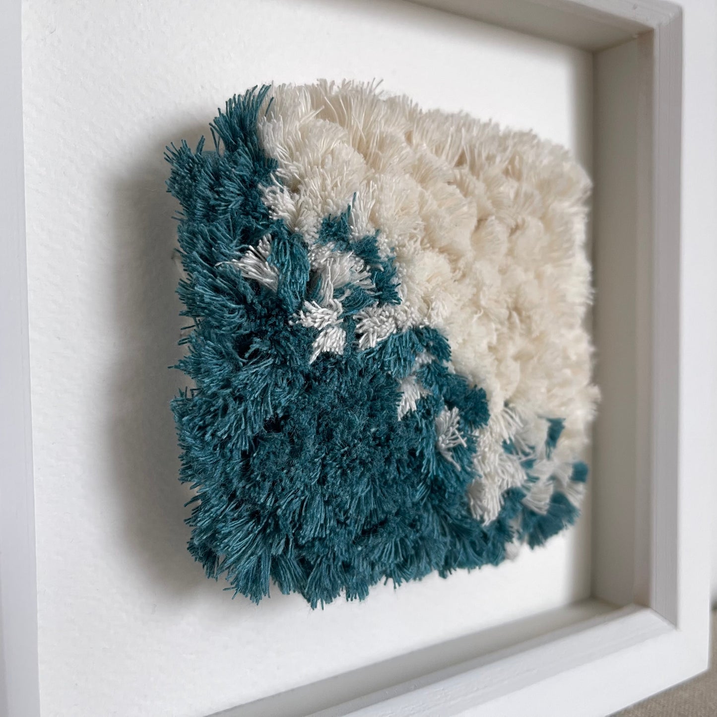 Close up detail of teal and cream fluffy textured woven textile art in a square white painted wood frame