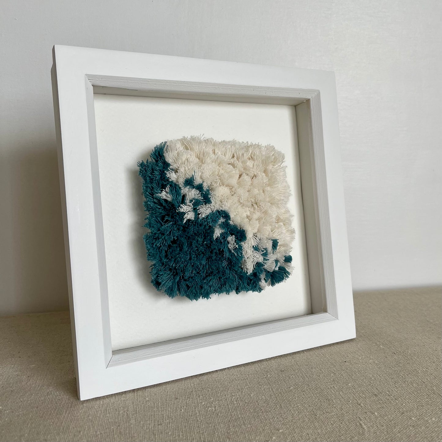 Teal and cream fluffy textured woven textile art in a square white painted wood deep box frame