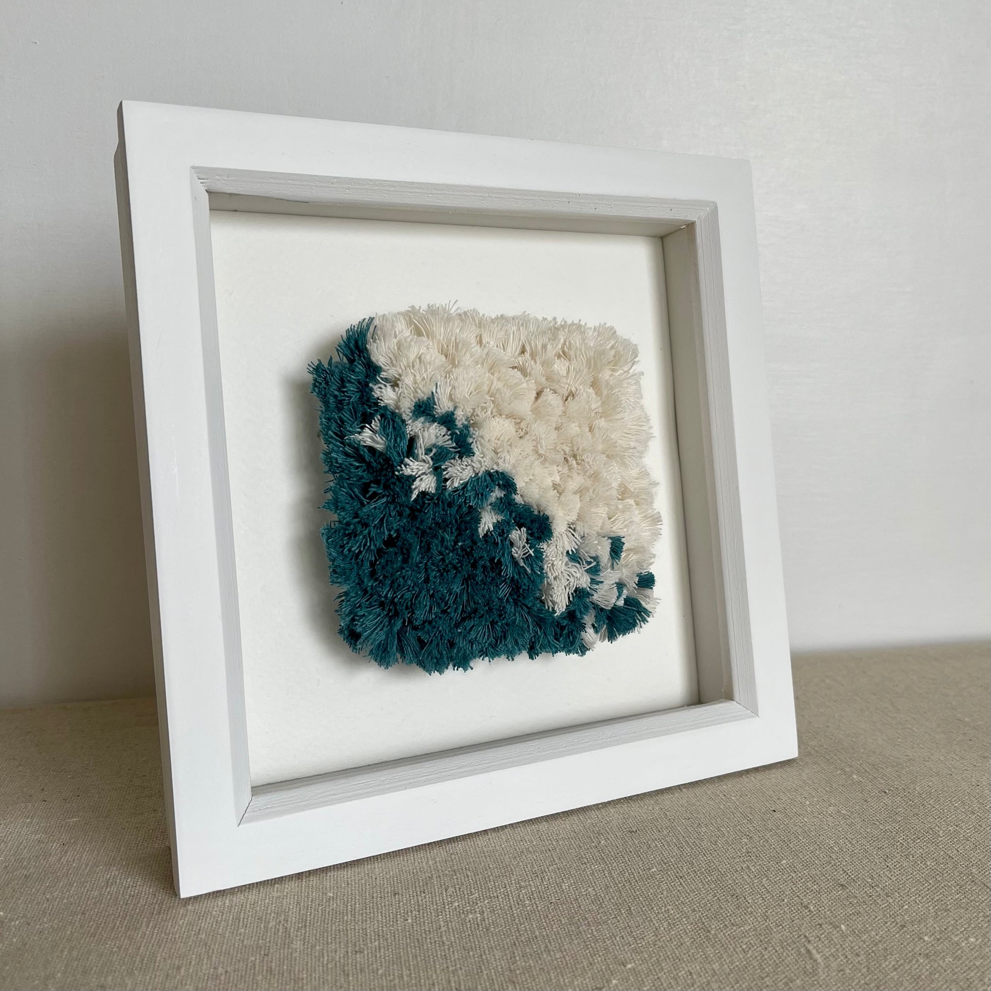 Teal and cream fluffy textured woven textile art in a square white painted wood deep box frame