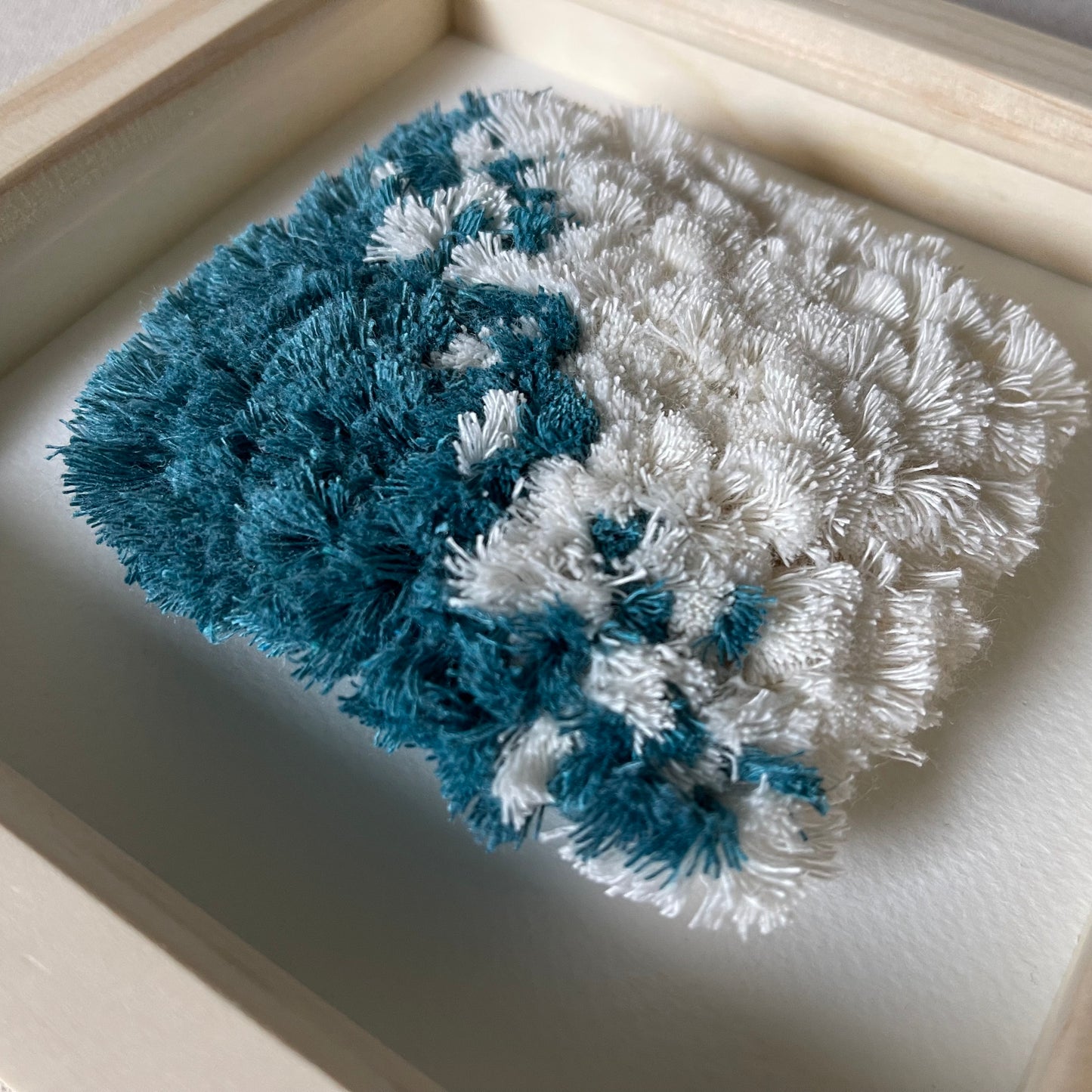 Close up detail of teal and cream fluffy textured woven textile art in a square natural wood deep box frame